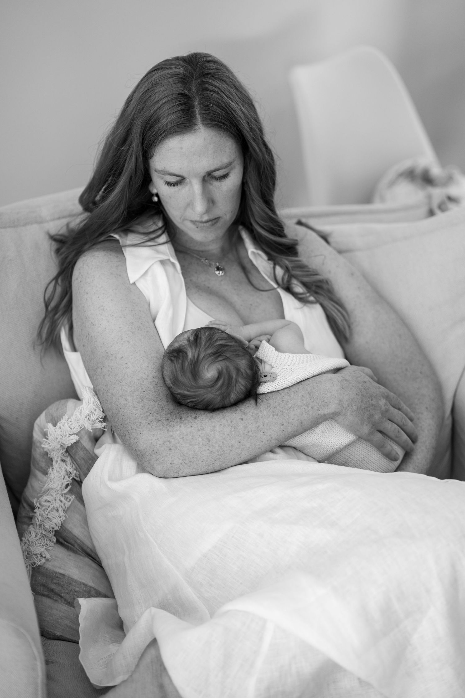 Black and white portrait of a mother tenderly cradling and nursing her newborn baby in a chair.