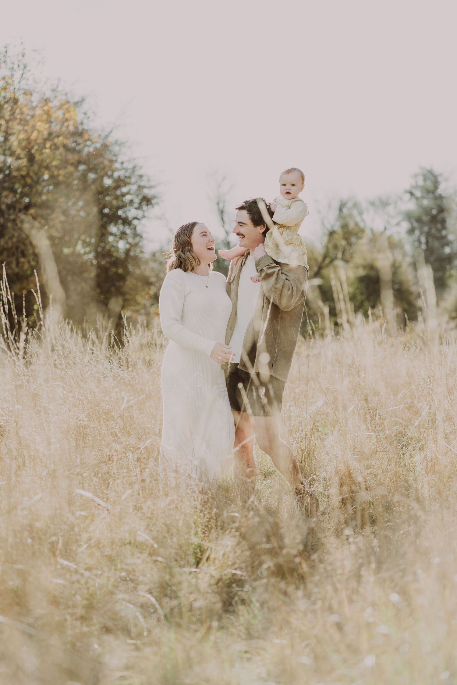 A family shares tender moments together in a sun-lit field of tall golden grass.