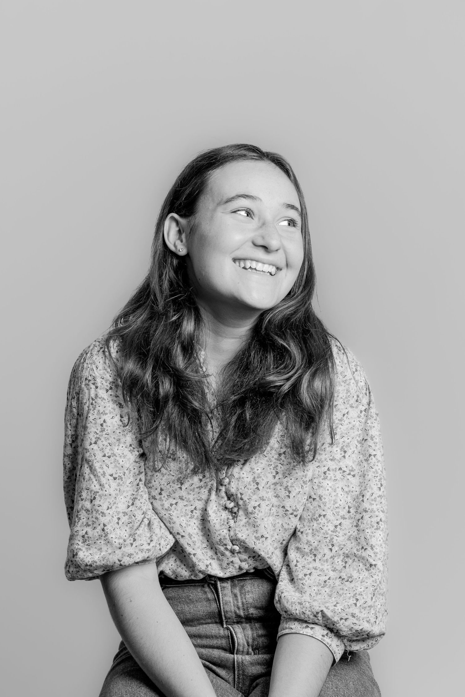 Black and white portrait of a smiling teenage girl with long wavy hair wearing a floral blouse.
