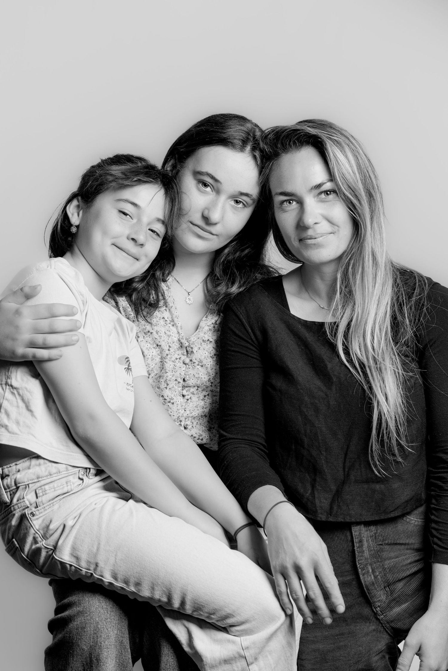 Three females pose together warmly in a black and white family studio portrait.