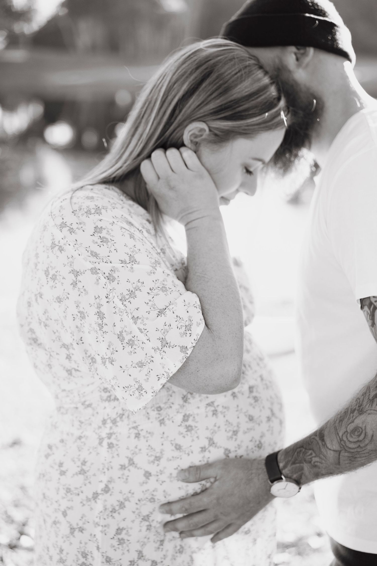 Intimate black and white maternity photo of couple tenderly touching pregnant belly outdoors.
