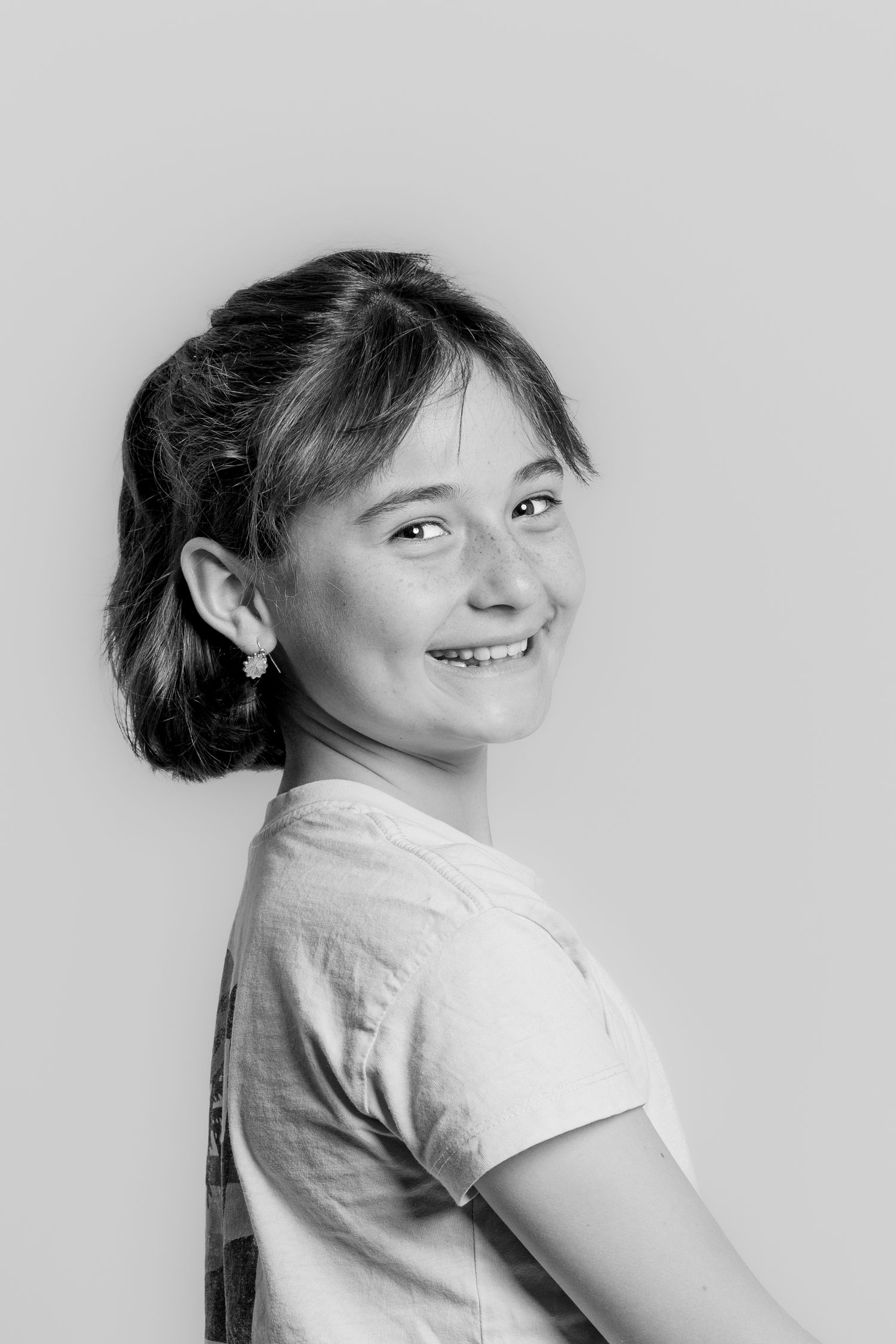 A smiling young girl poses sideways in a black and white studio portrait.