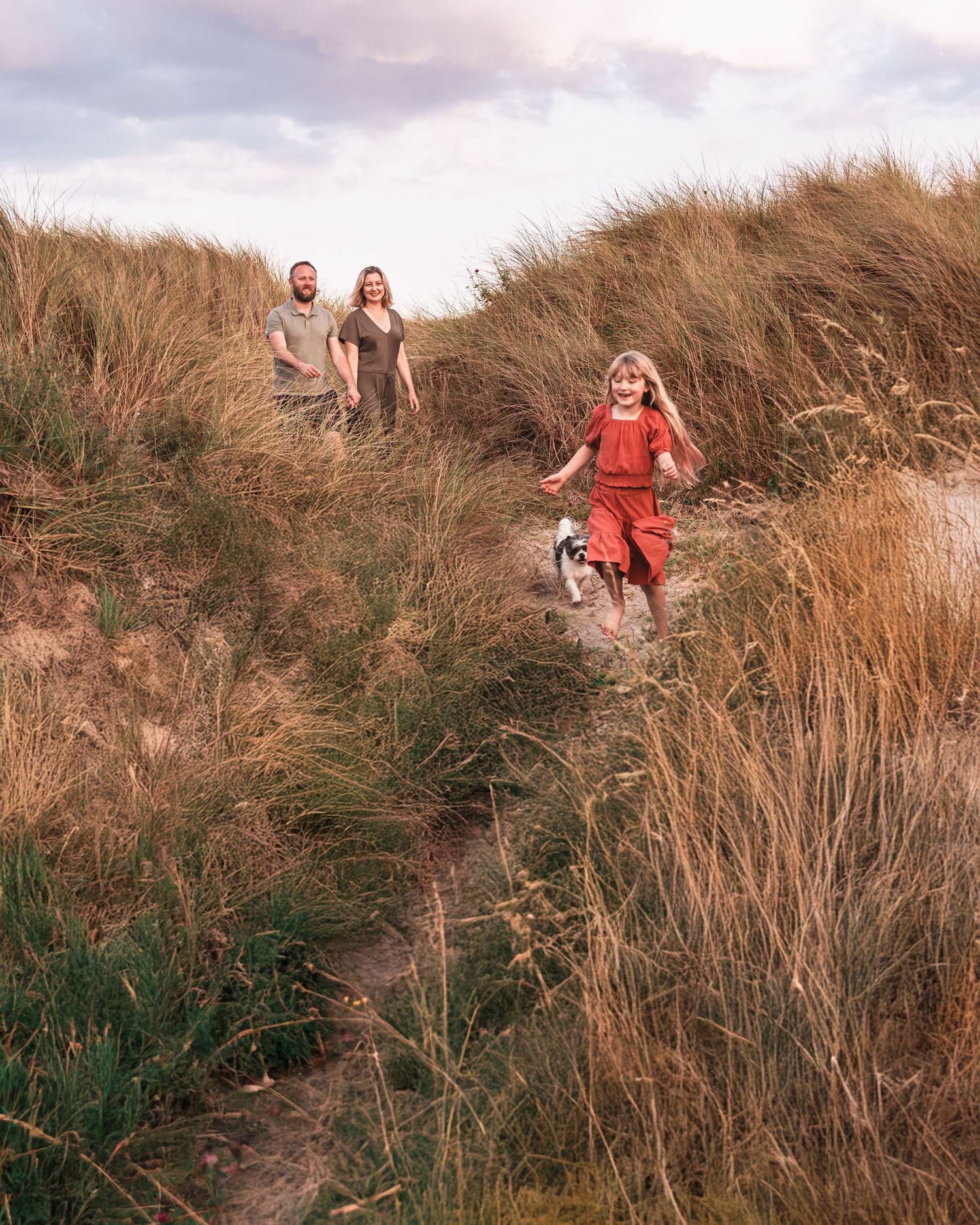 Family walking through sandy coastal path during sunset.
