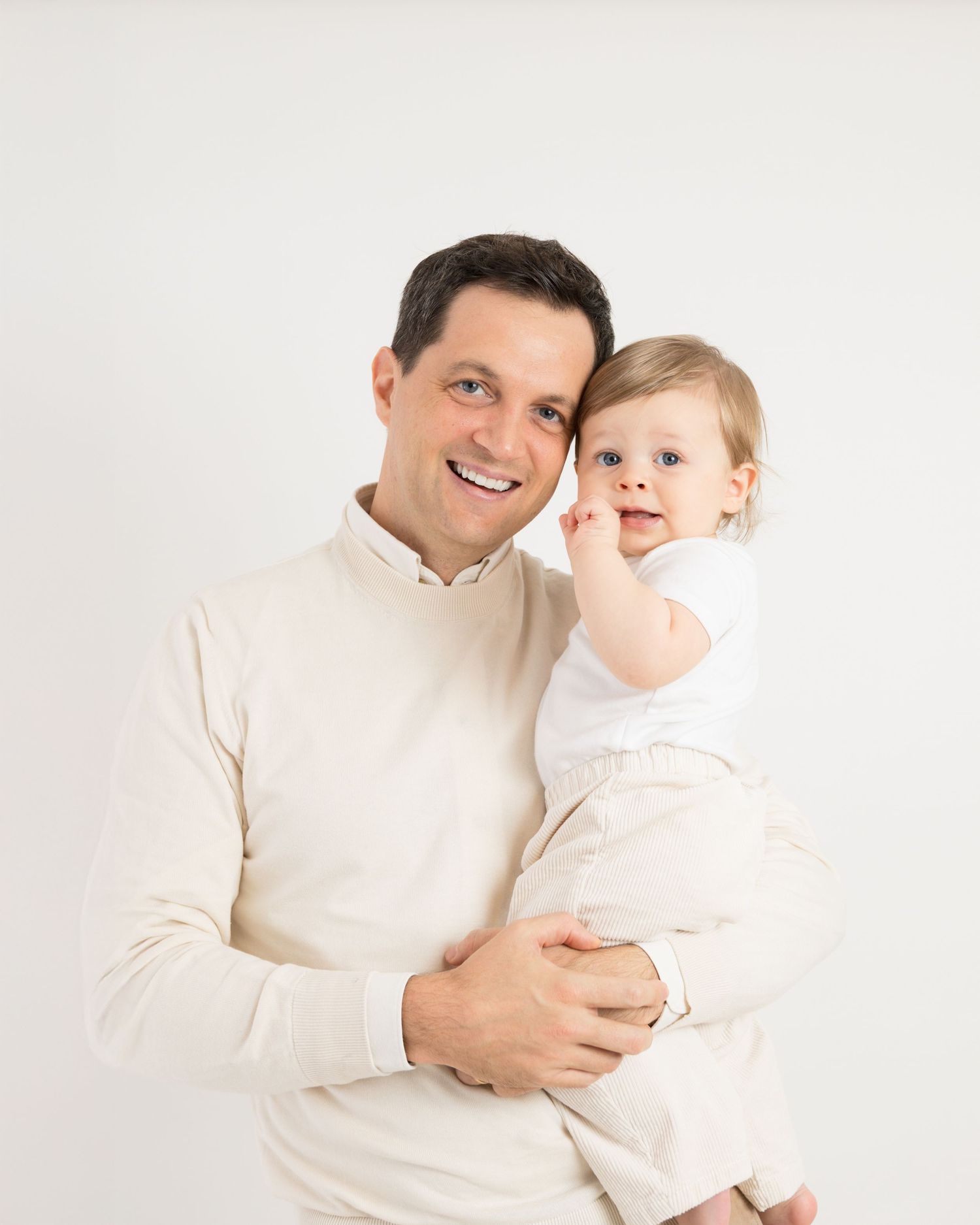 A parent and child wearing white sweaters share tender moments in a bright studio setting.