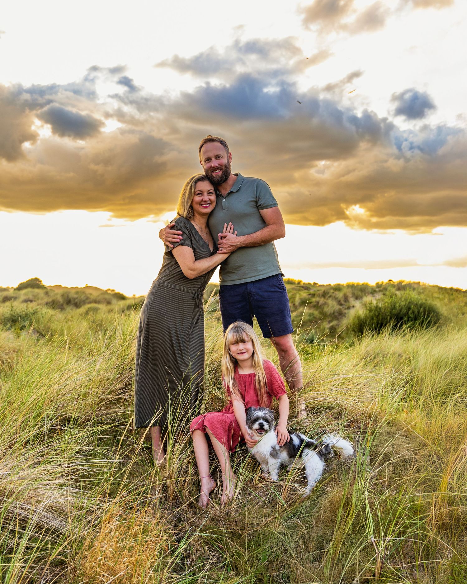 Family and dog enjoying sunset together in tall beach grass dunes during golden hour photography session.