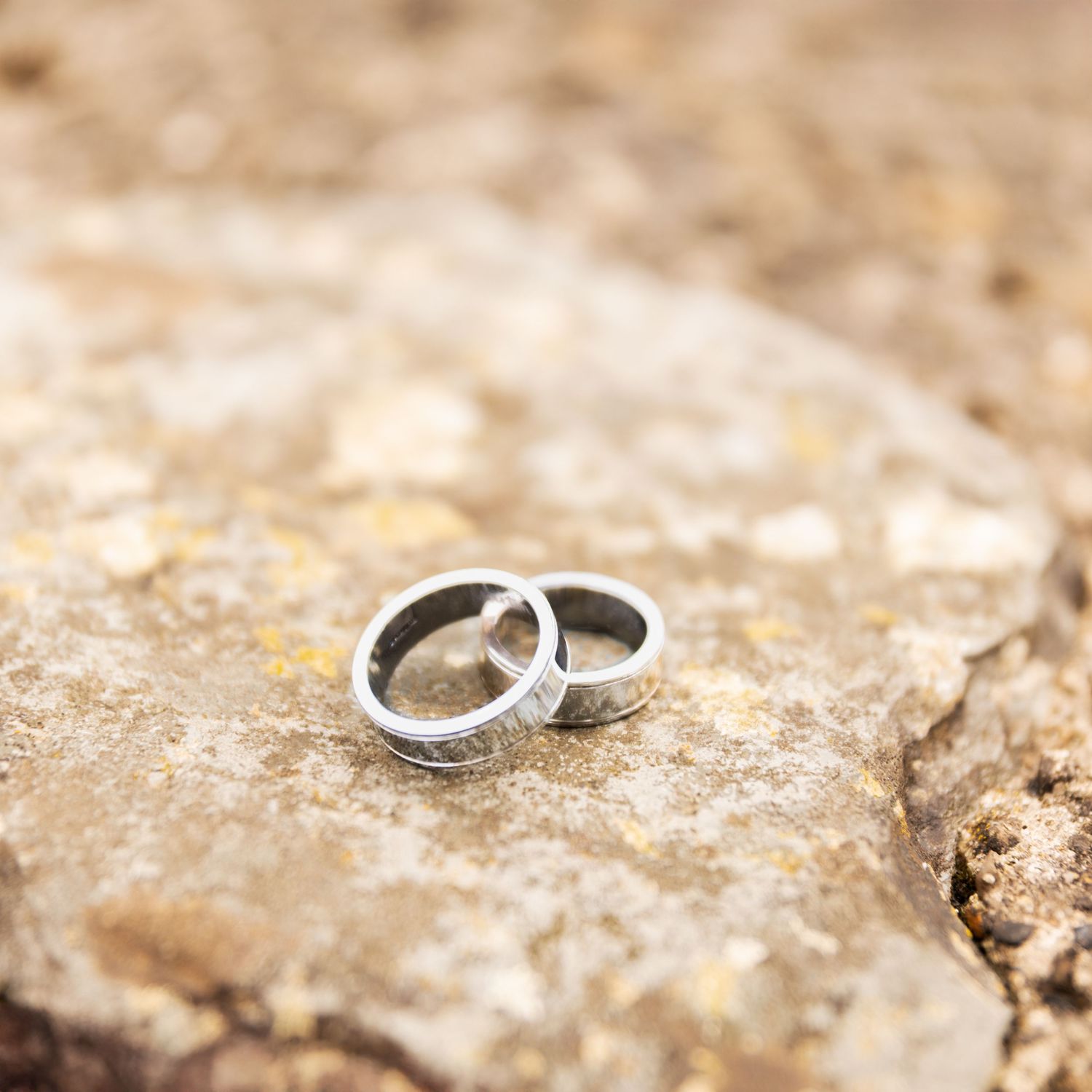 Two silver wedding bands resting on a textured stone surface, symbolizing love and commitment.