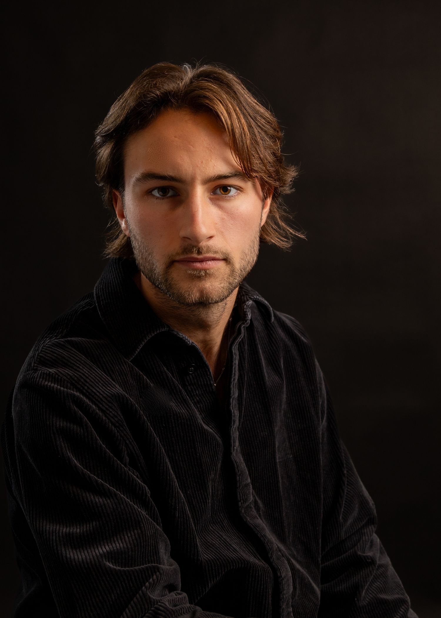 Portrait of person in black corduroy jacket against dark background.