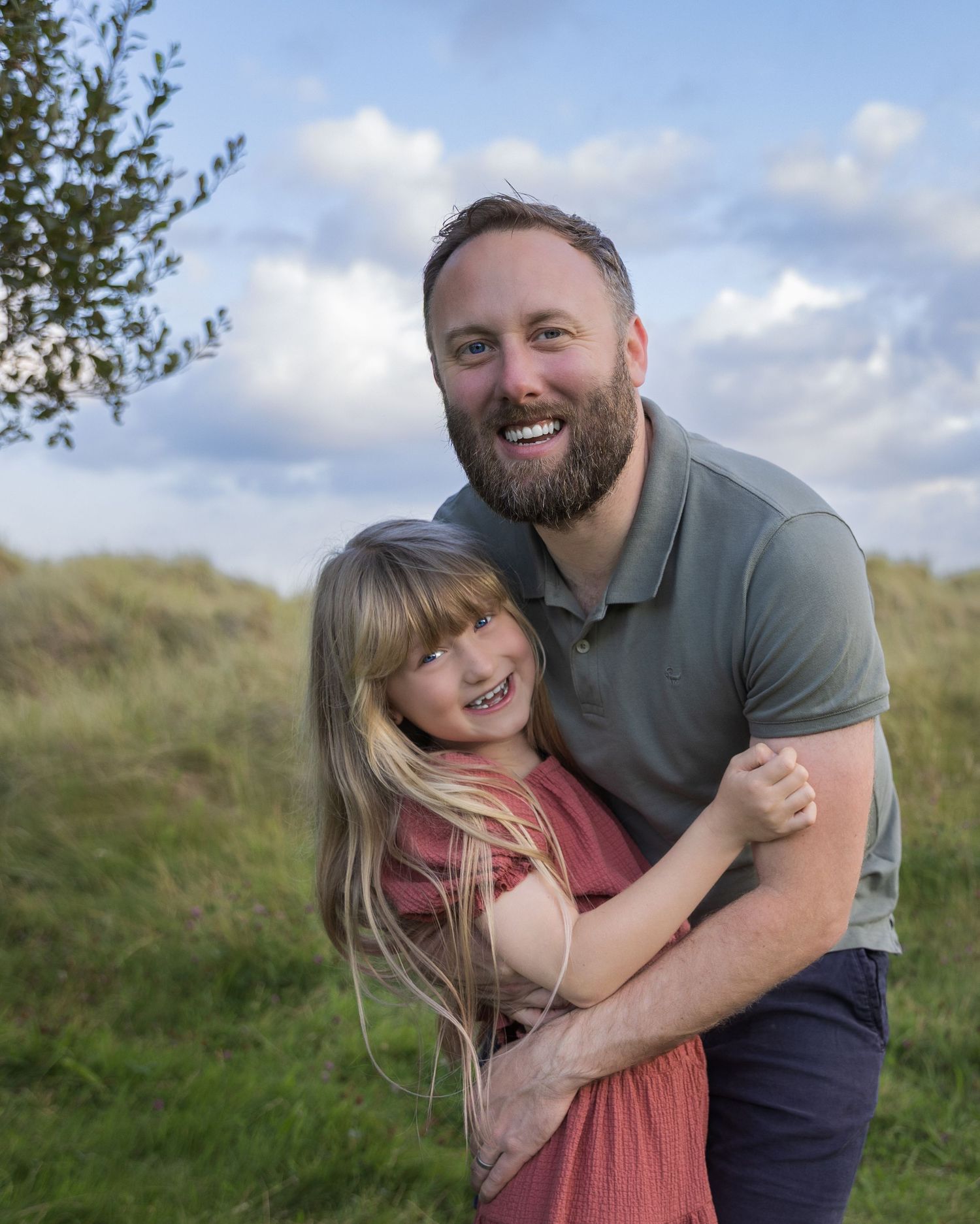 A joyful family moment captured in a grassy field during golden hour with natural expressions and laughter.