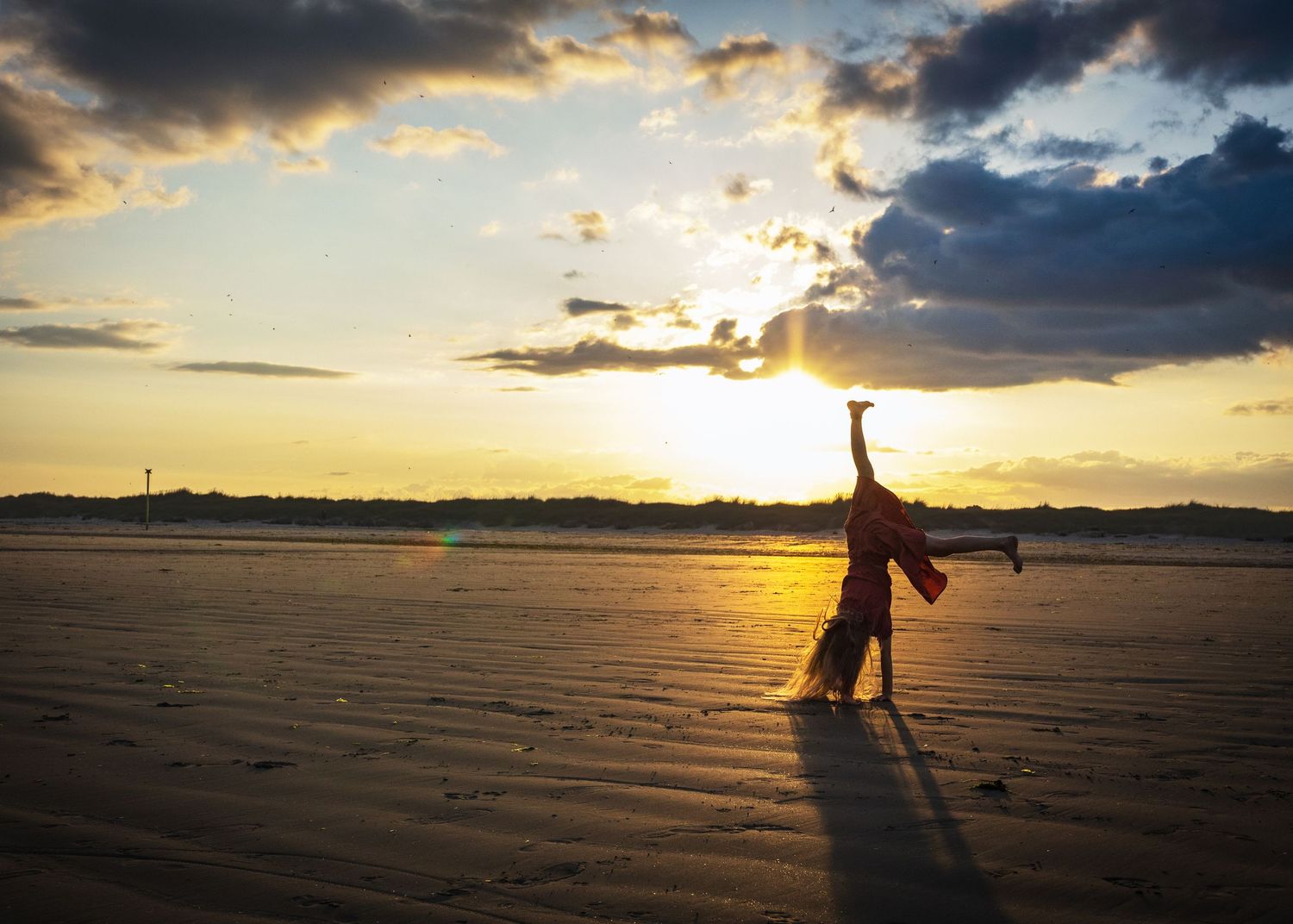 Dramatic sunset silhouettes against rippling water on a beach.