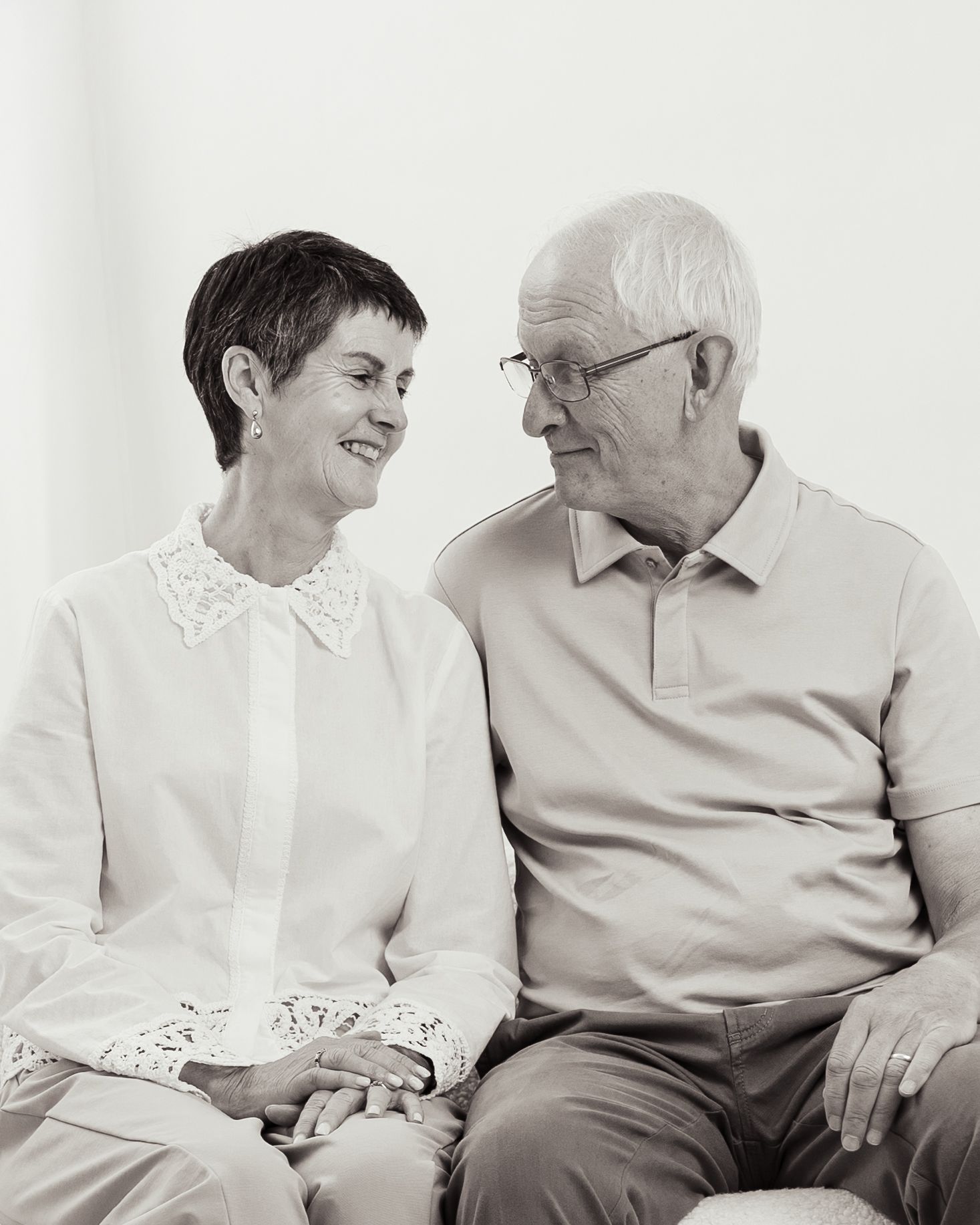 Two people in white and gray clothing share an intimate moment on a white background.