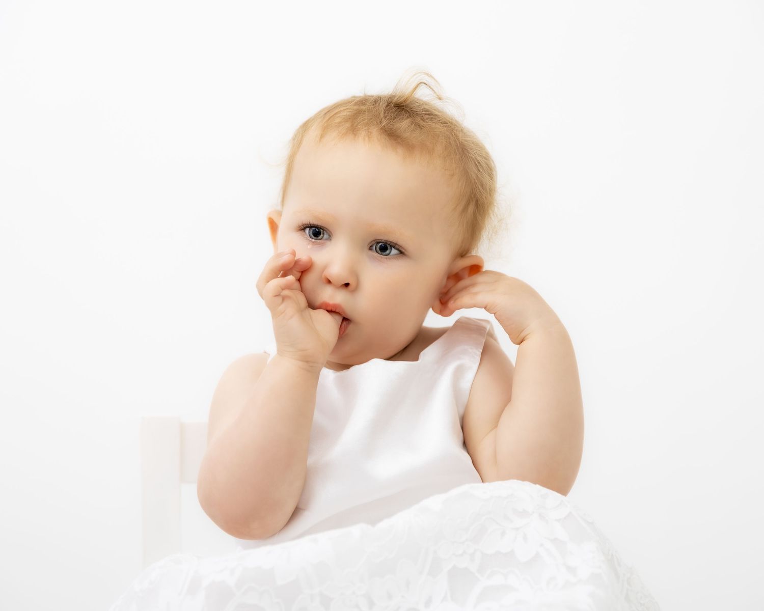 Baby in white dress exploring and playing against bright background.