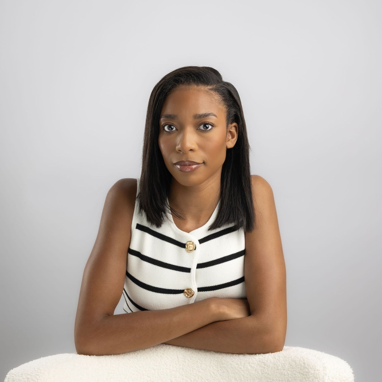 Young woman in striped sleeveless top with arms crossed, posing confidently against a light gray background.