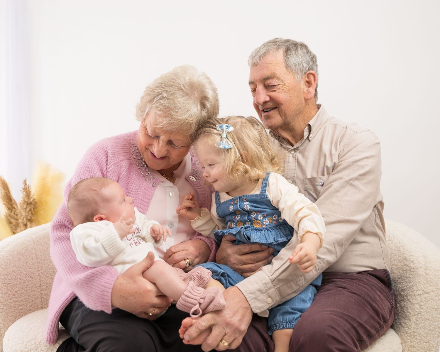 Elderly couples sitting together on white couch sharing tender moments.
