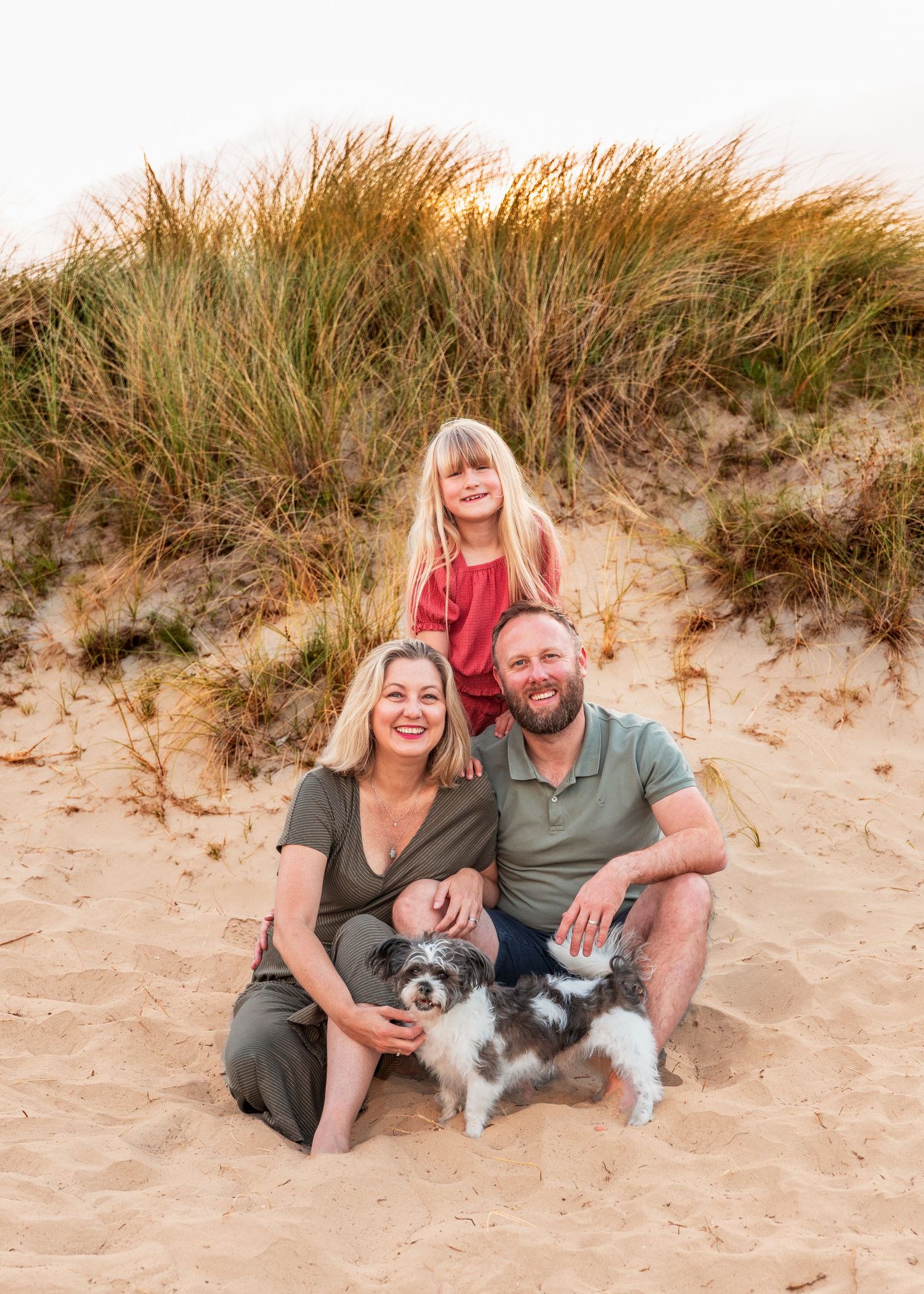 Family portrait session on sandy beach with small dog.