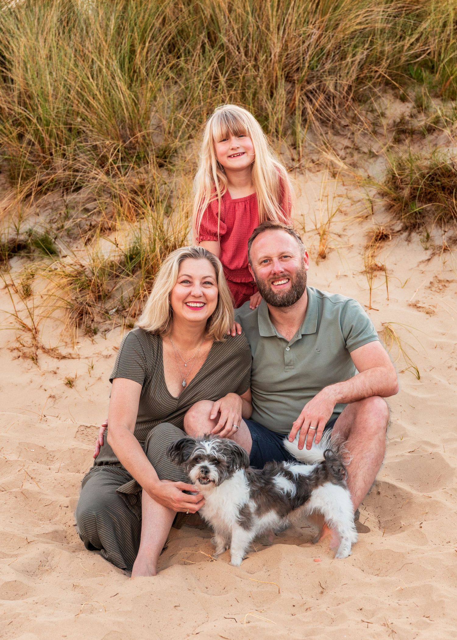 Couple relaxing on beach sand with their small fluffy dog.