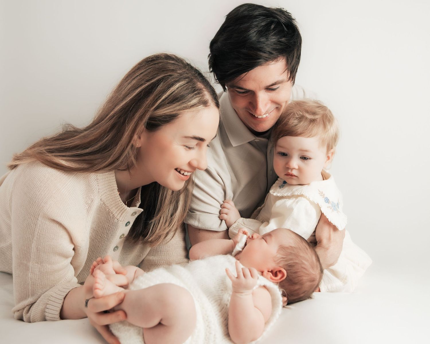 Happy young family with two children, parents smiling at newborn baby while toddler watches, white background.
