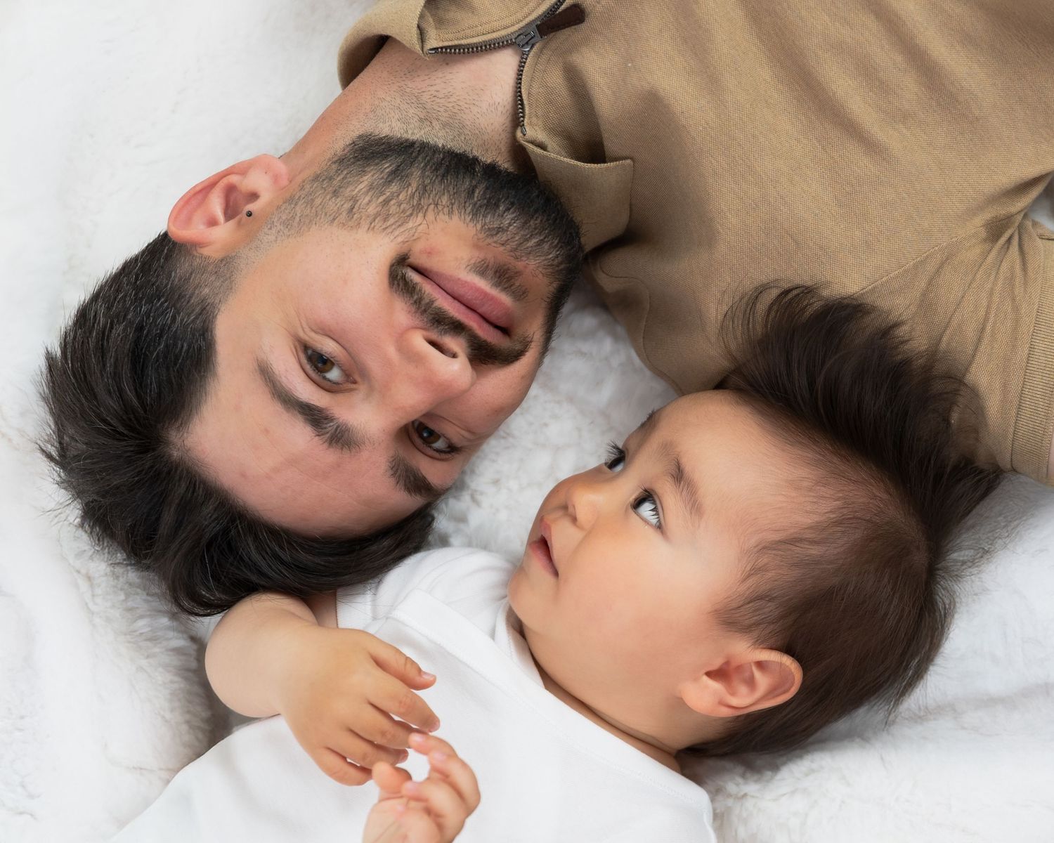 Parent and baby lying on white background sharing playful moments.