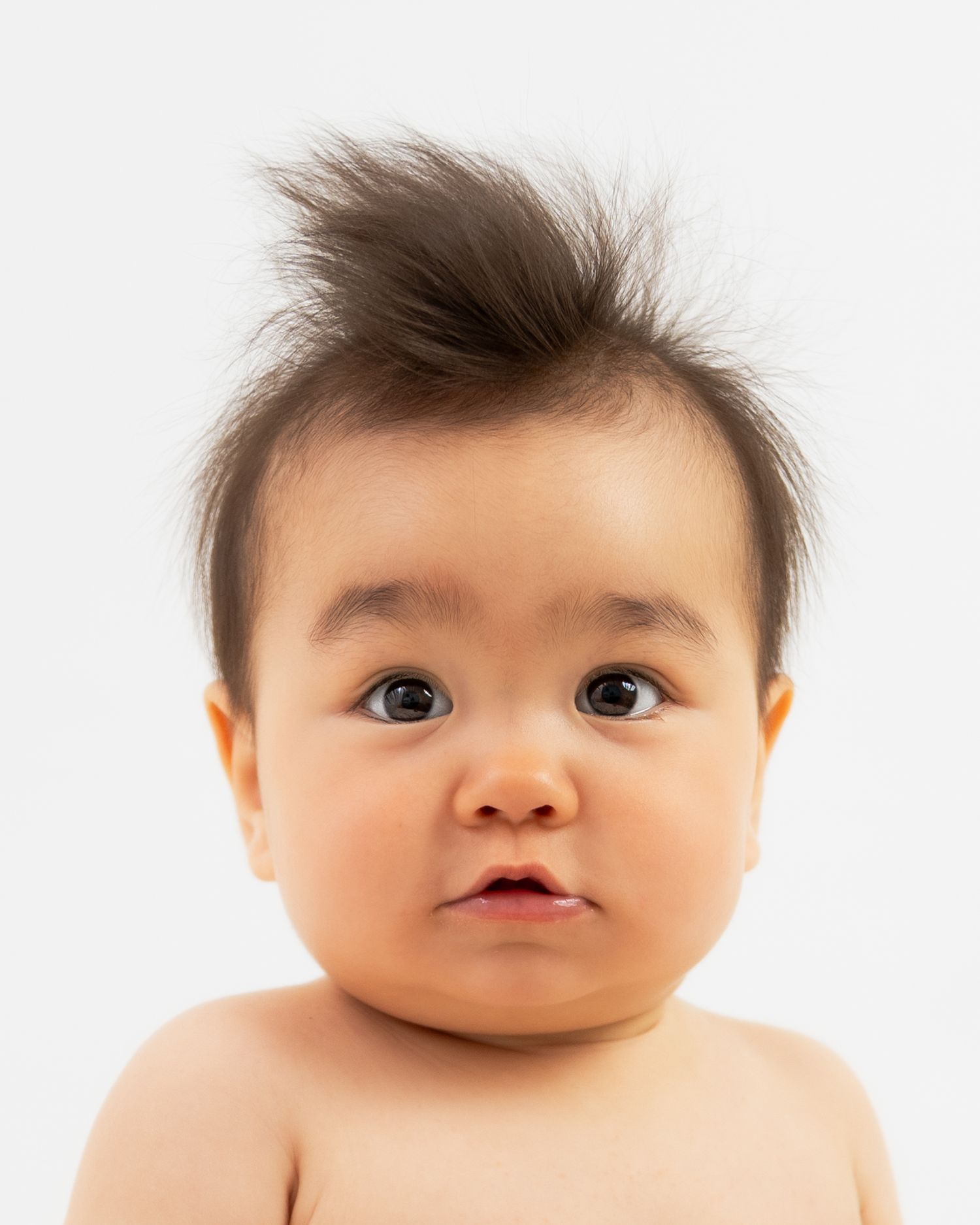 Adorable Asian baby with spiky dark hair and chubby cheeks posing for a portrait against white background.