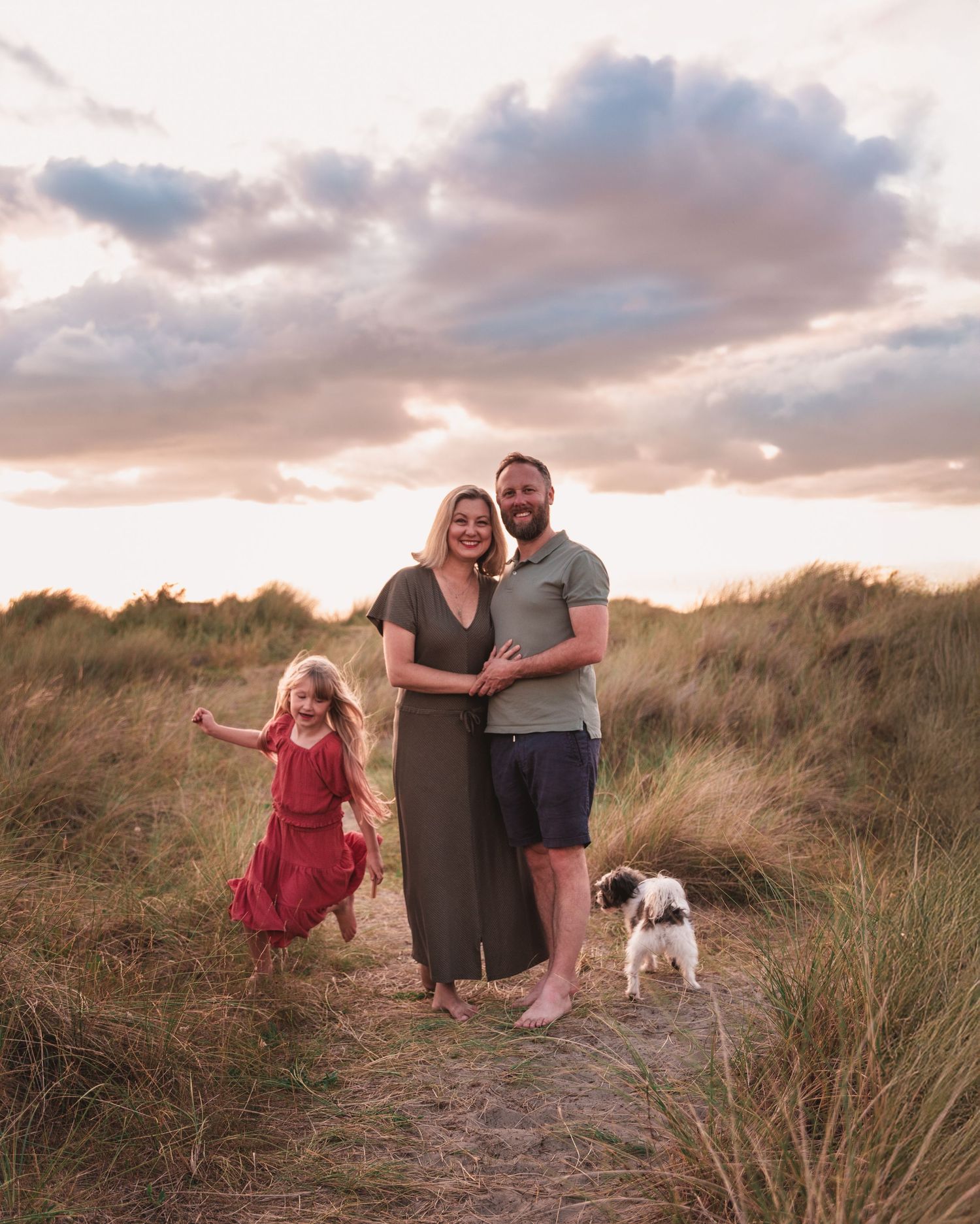 Group relaxing among coastal dunes with small dog during sunset photo session.