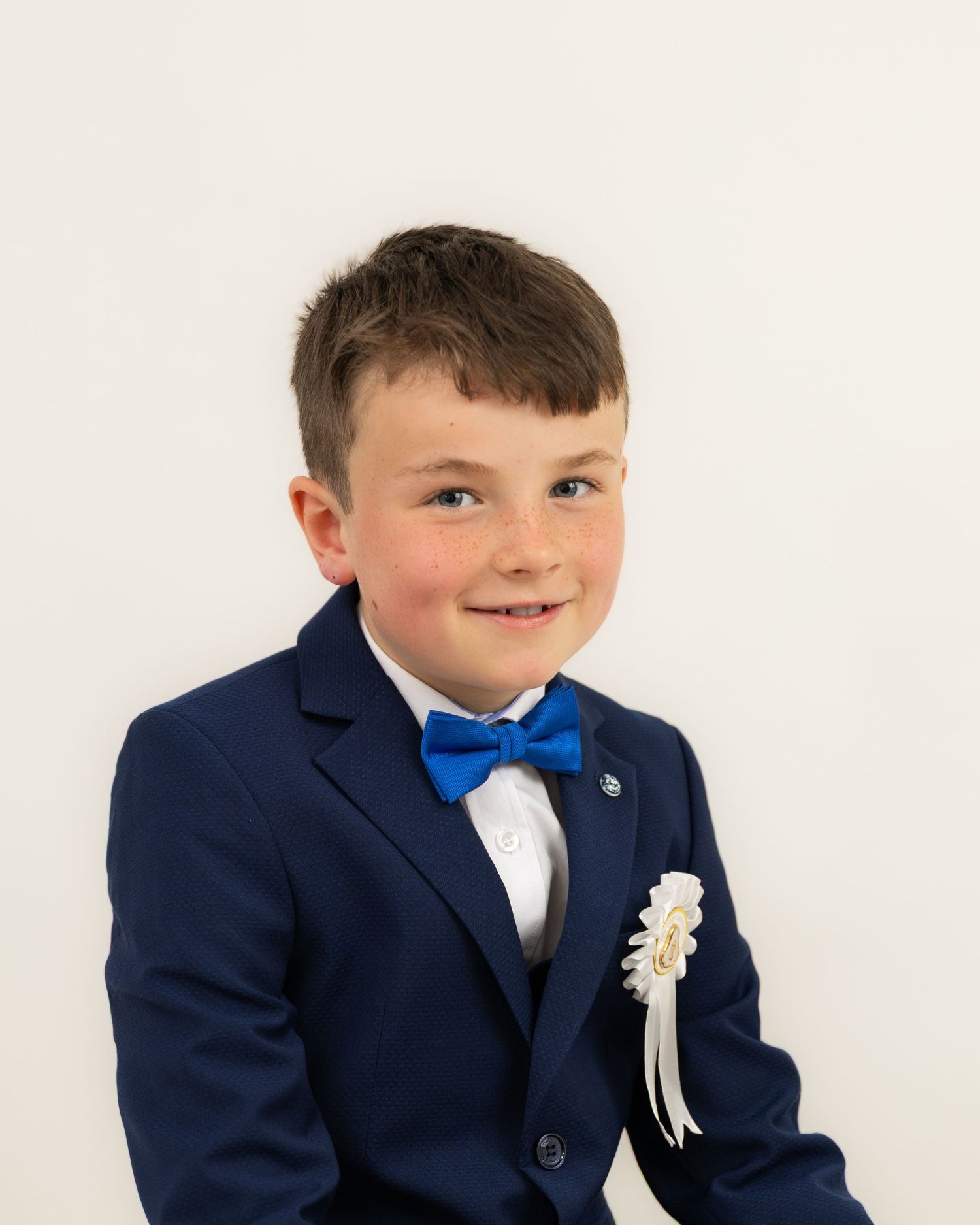 A young boy in a navy suit and blue bowtie posing formally.