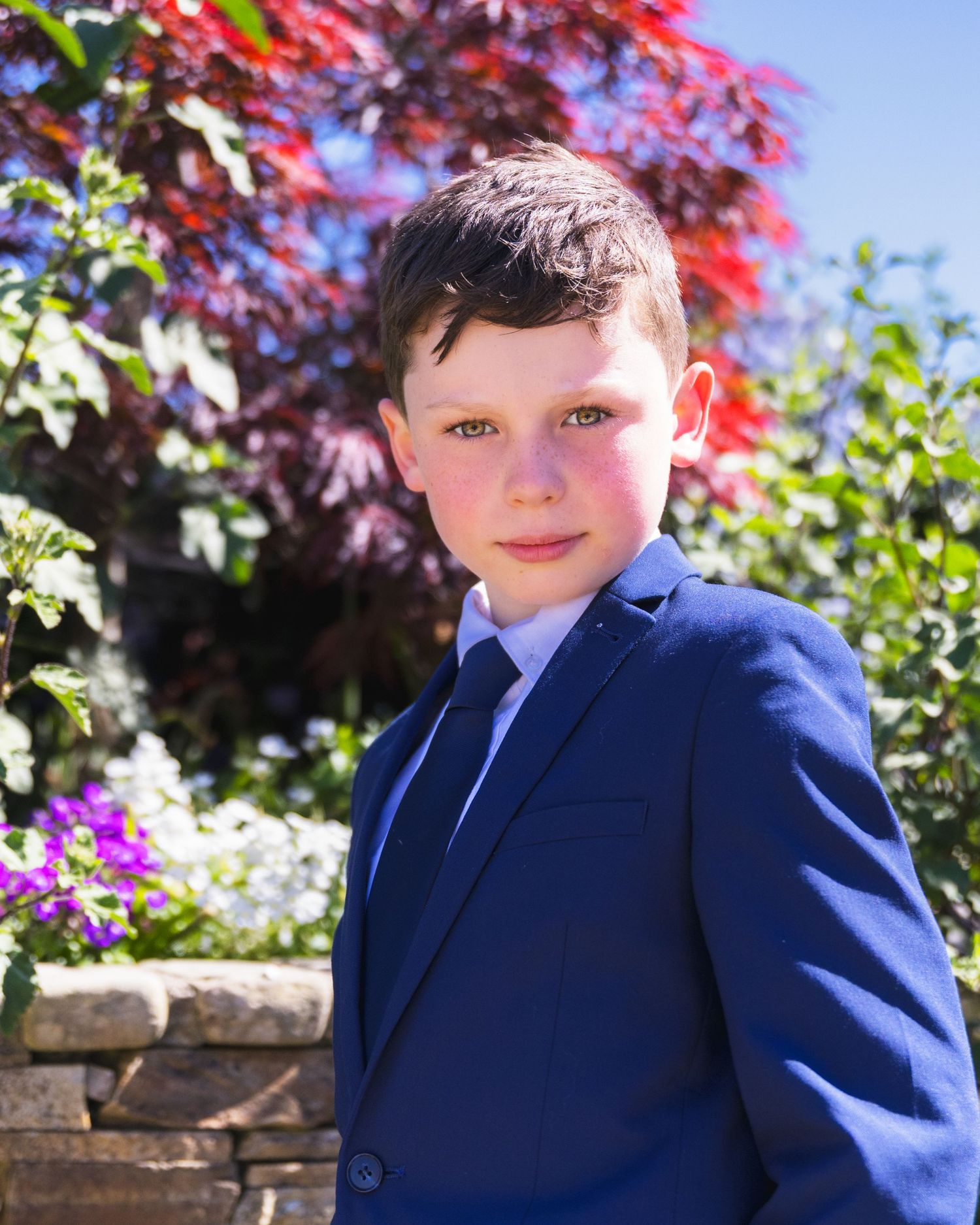 Young boys in navy suits smiling against a colorful garden backdrop.