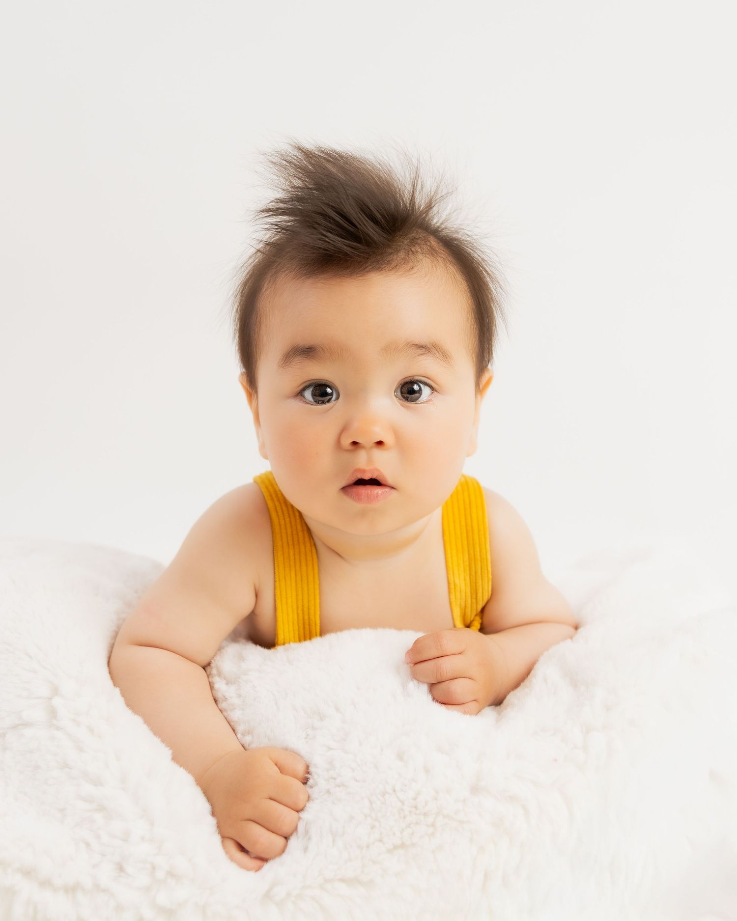 Baby wearing yellow outfit lying on white textured blanket.