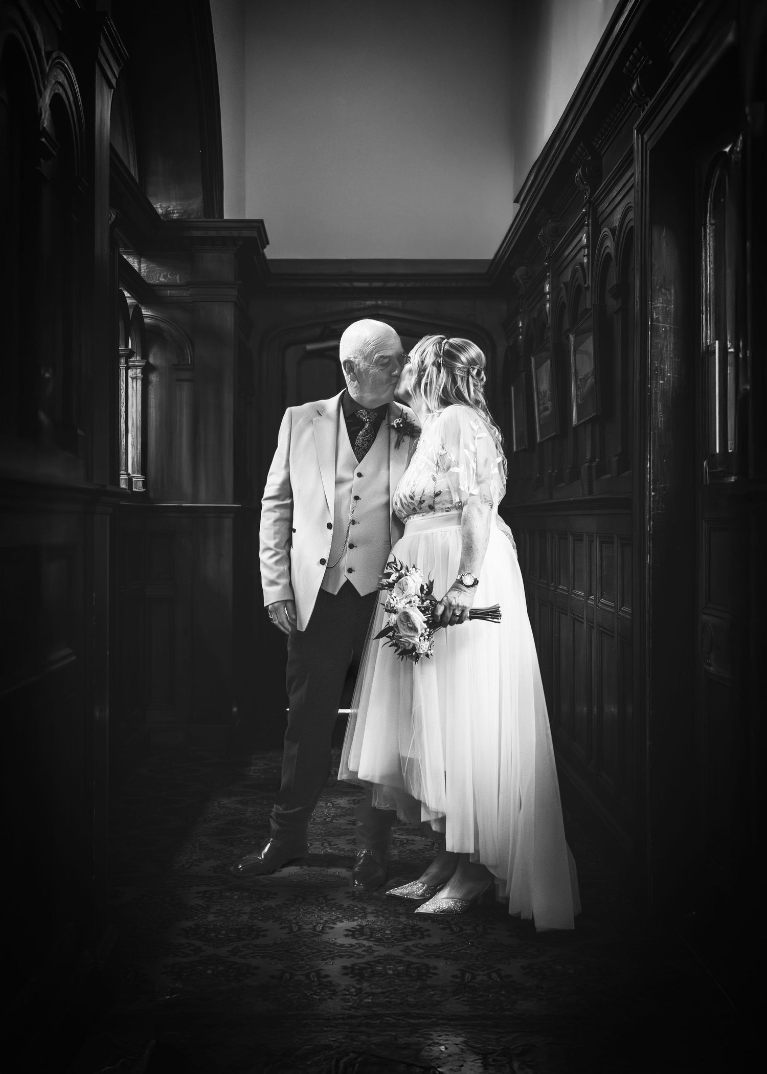 A black and white wedding photo showing a couple in a dark hallway with vintage architectural details.