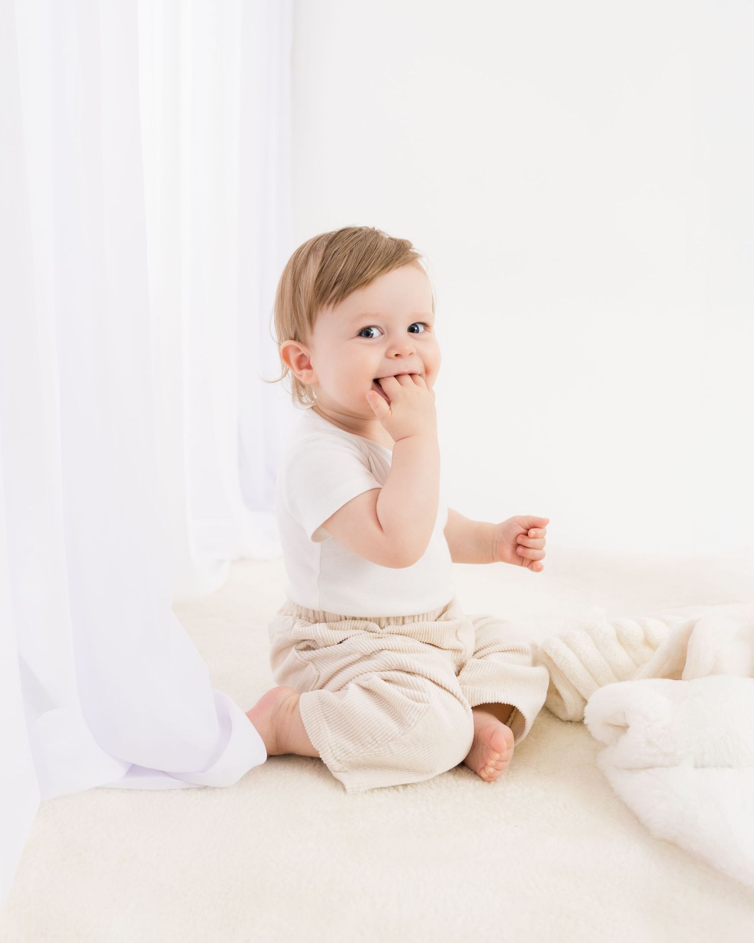 Baby in cream-colored outfit lying on white bedding shows various playful expressions and poses.