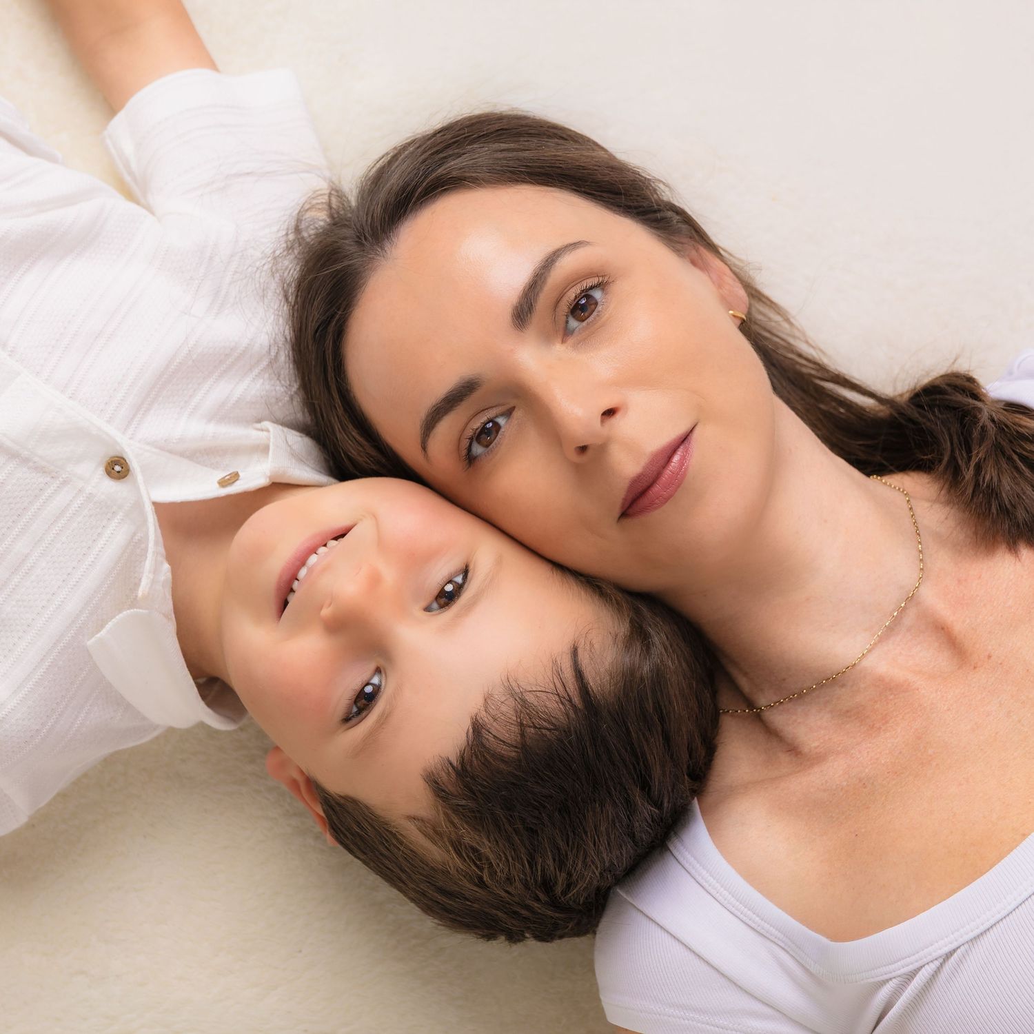 A woman and child lying down together, heads touching, smiling warmly in a tender mother-son portrait.