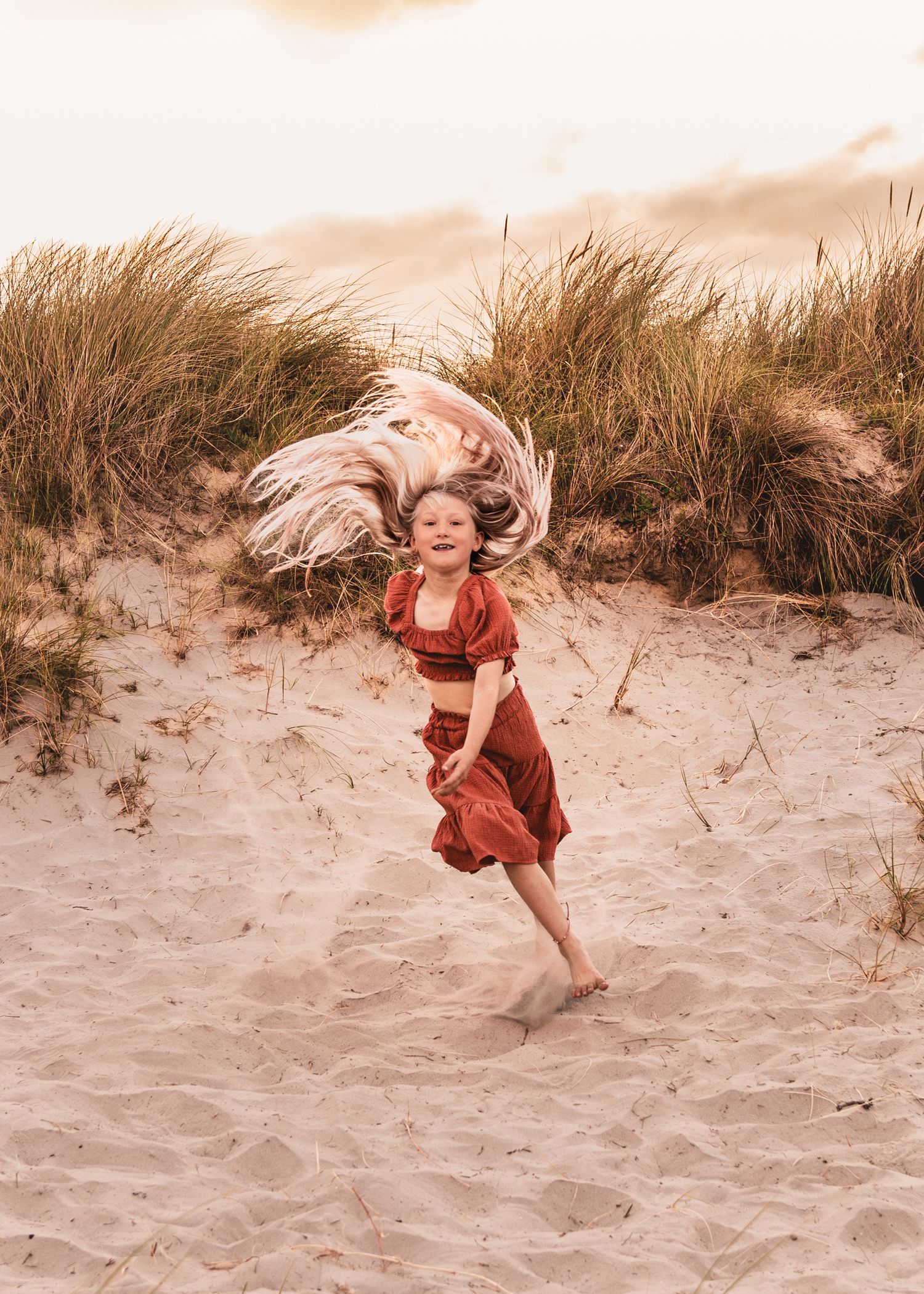 Child playing and jumping in sand dunes during golden hour.