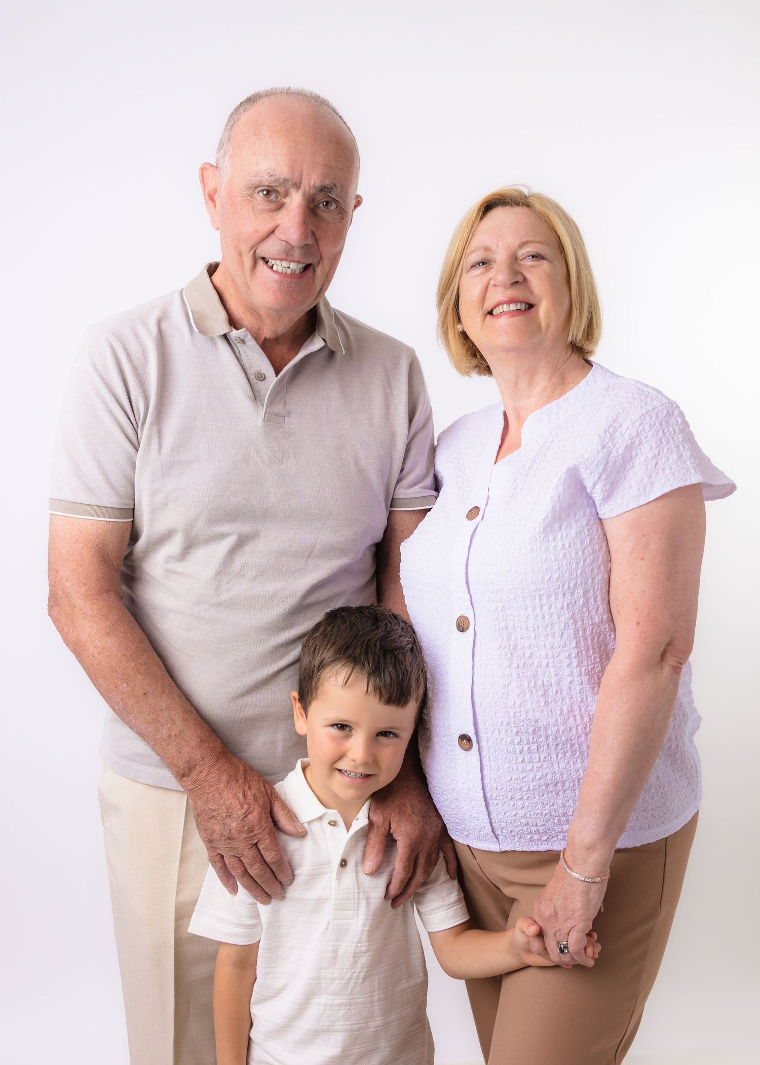 Grandparents smiling with young grandson in a bright studio family portrait photo.