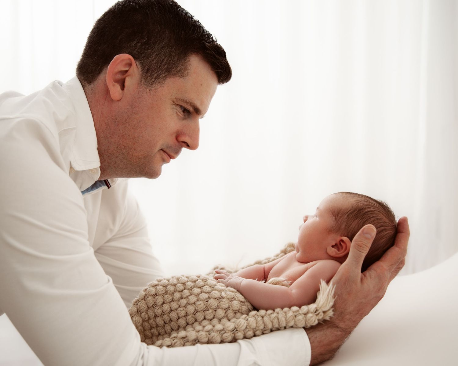 Tender moment between parent and newborn during professional portrait session.