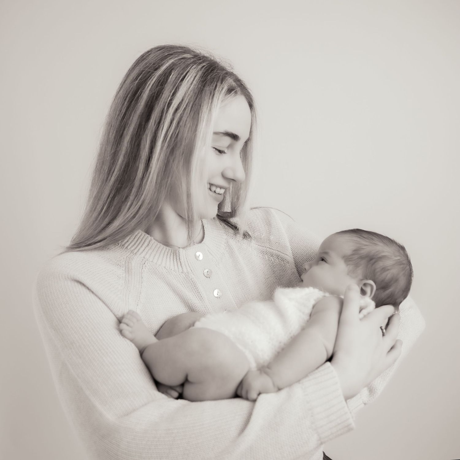 Black and white photo of a smiling young woman cradling a sleeping newborn baby in her arms.