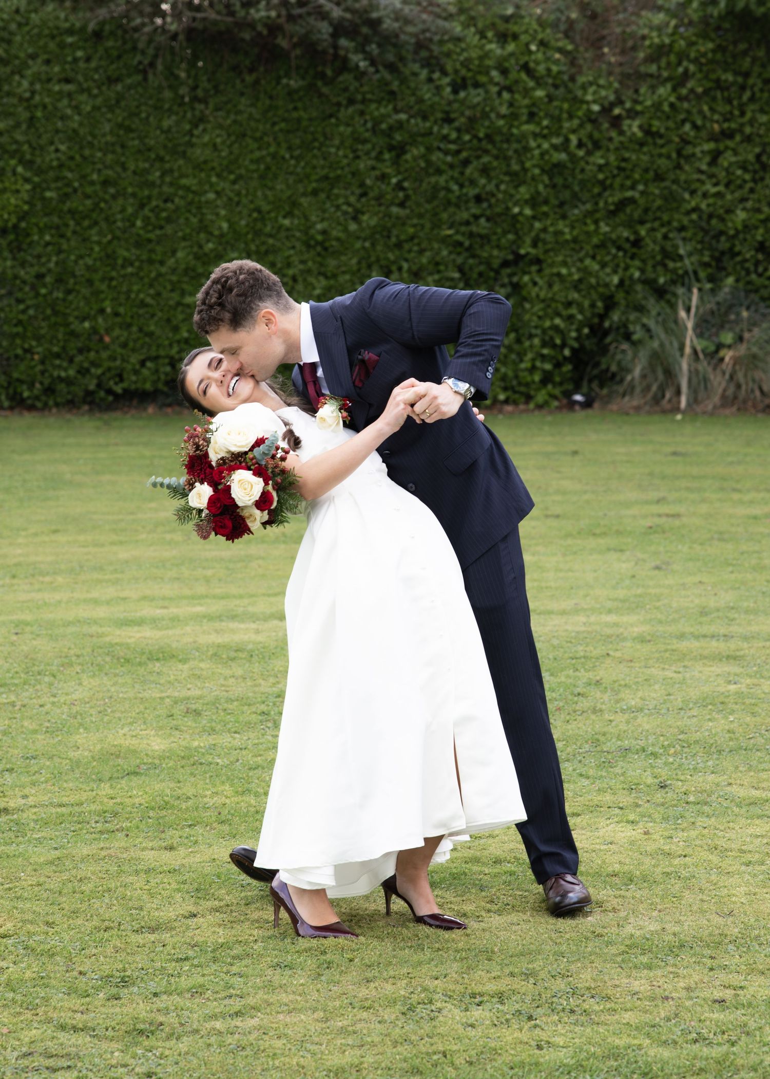 A romantic wedding couple performs a dip pose on a lush green lawn during their outdoor photo session.