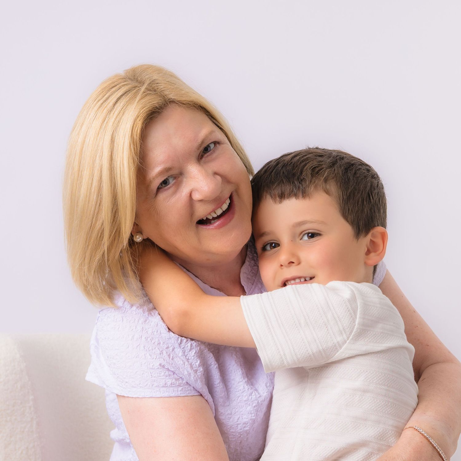 A smiling blonde woman hugging a happy young boy in a white studio portrait.