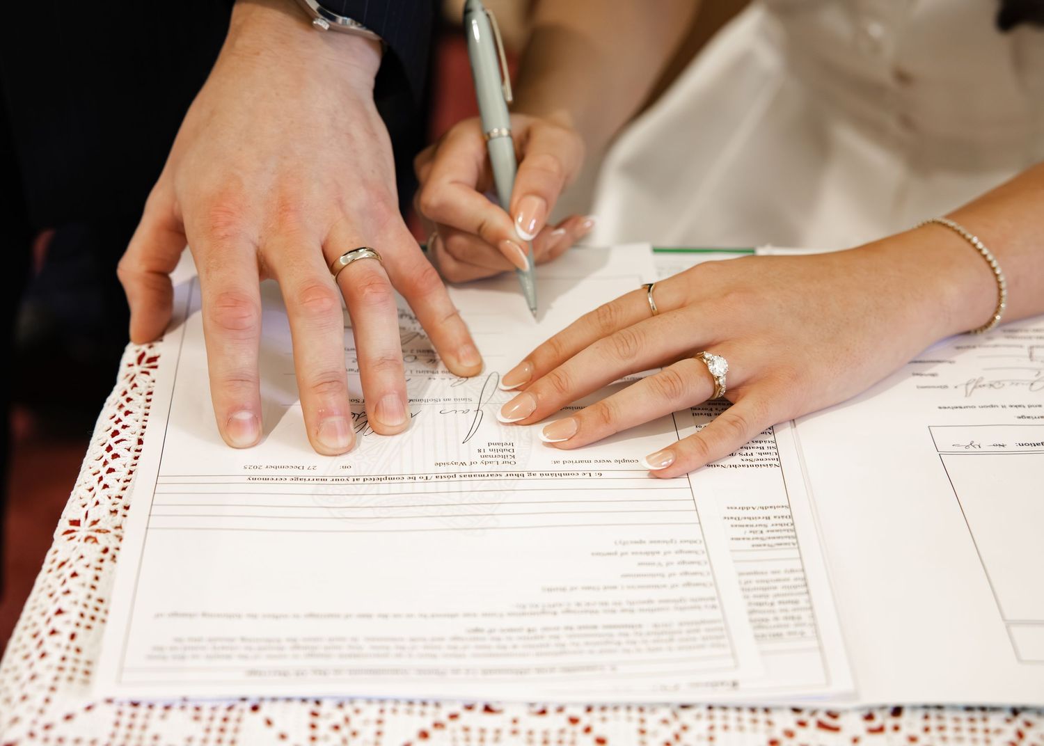 Newlywed couple signing marriage certificate with gold wedding rings visible on their hands.