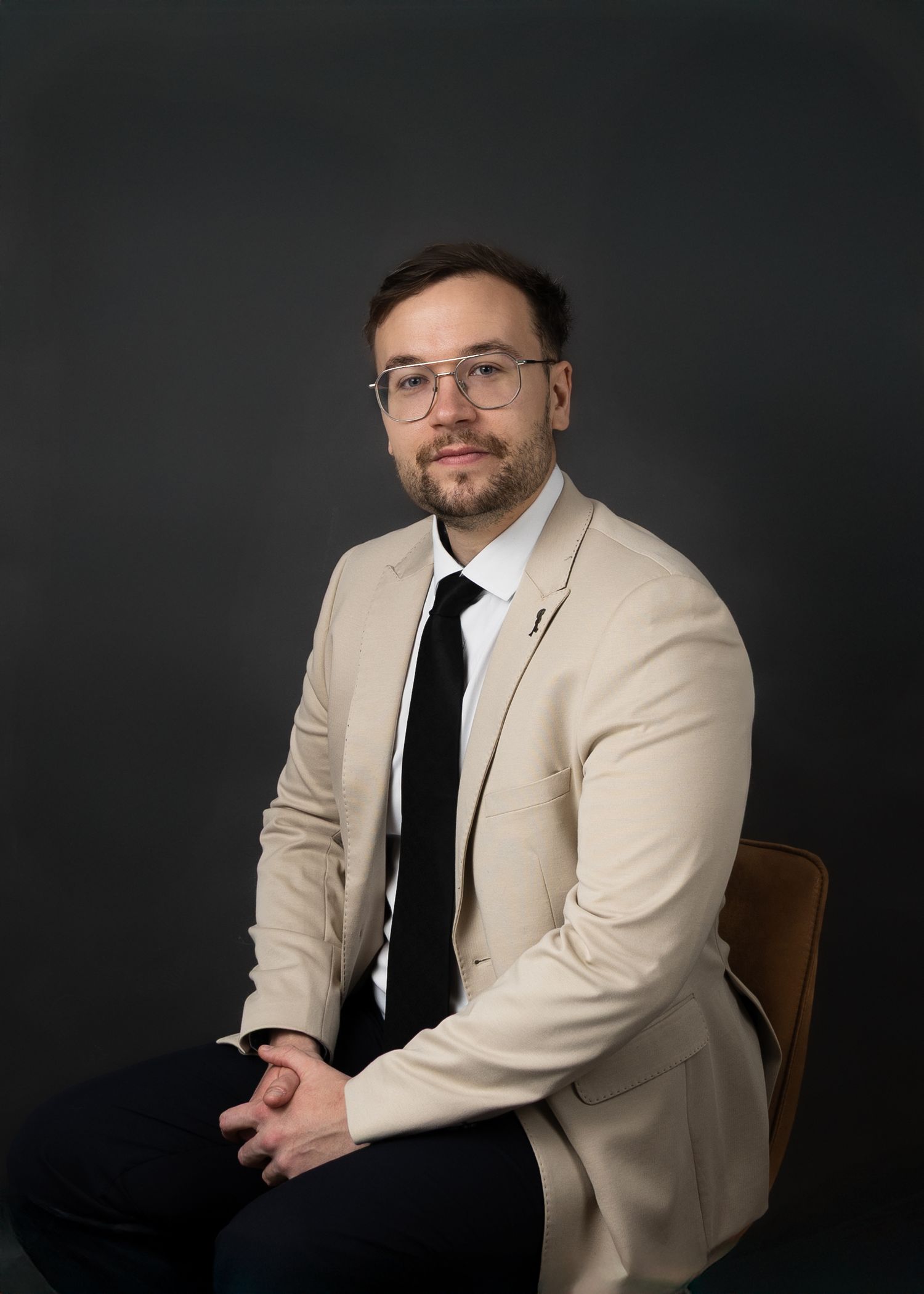 Business headshot series showing a person in beige jacket and black tie against dark background. Dublin Headshot