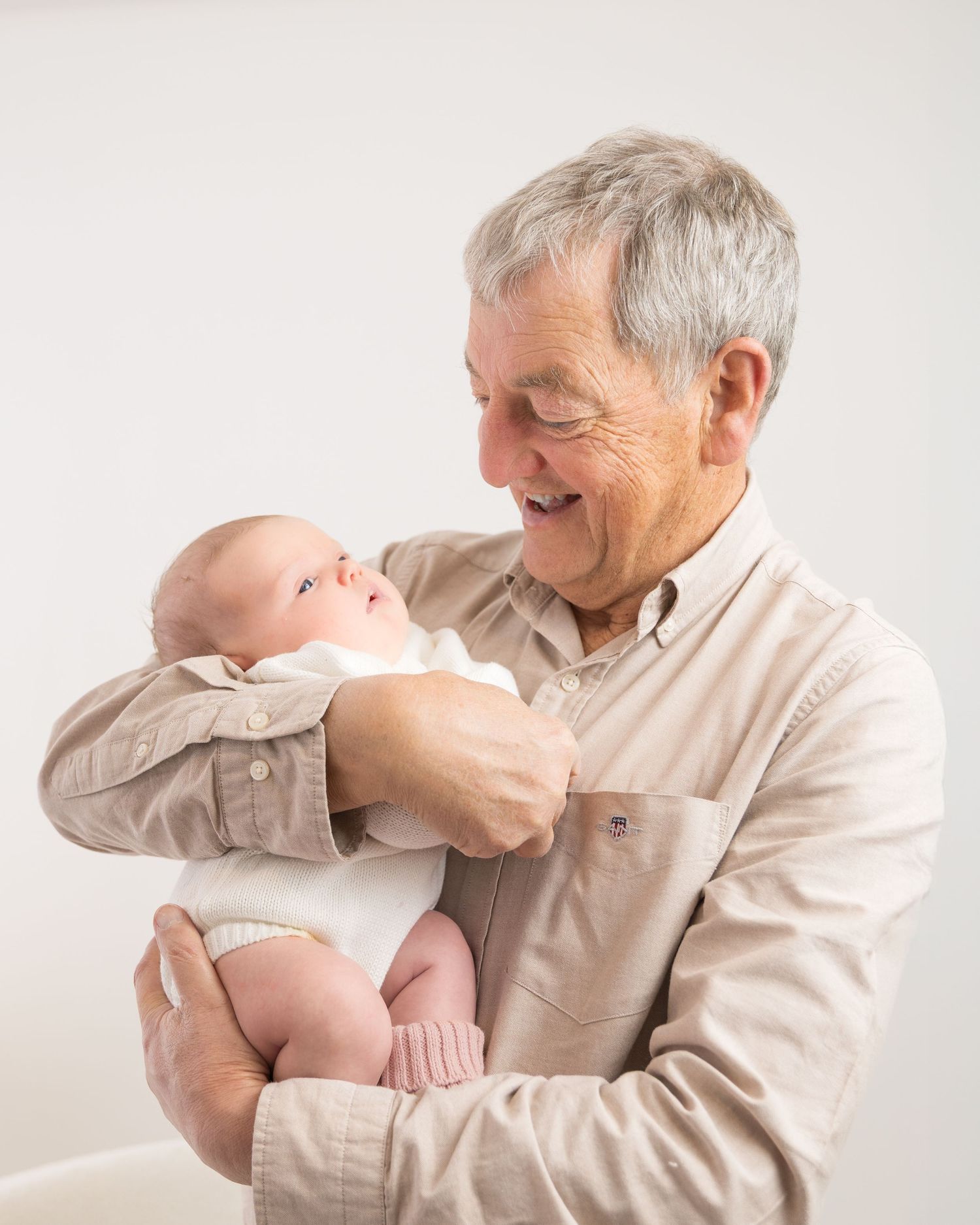 A tender moment shared between an elderly person and a newborn baby against a light background.