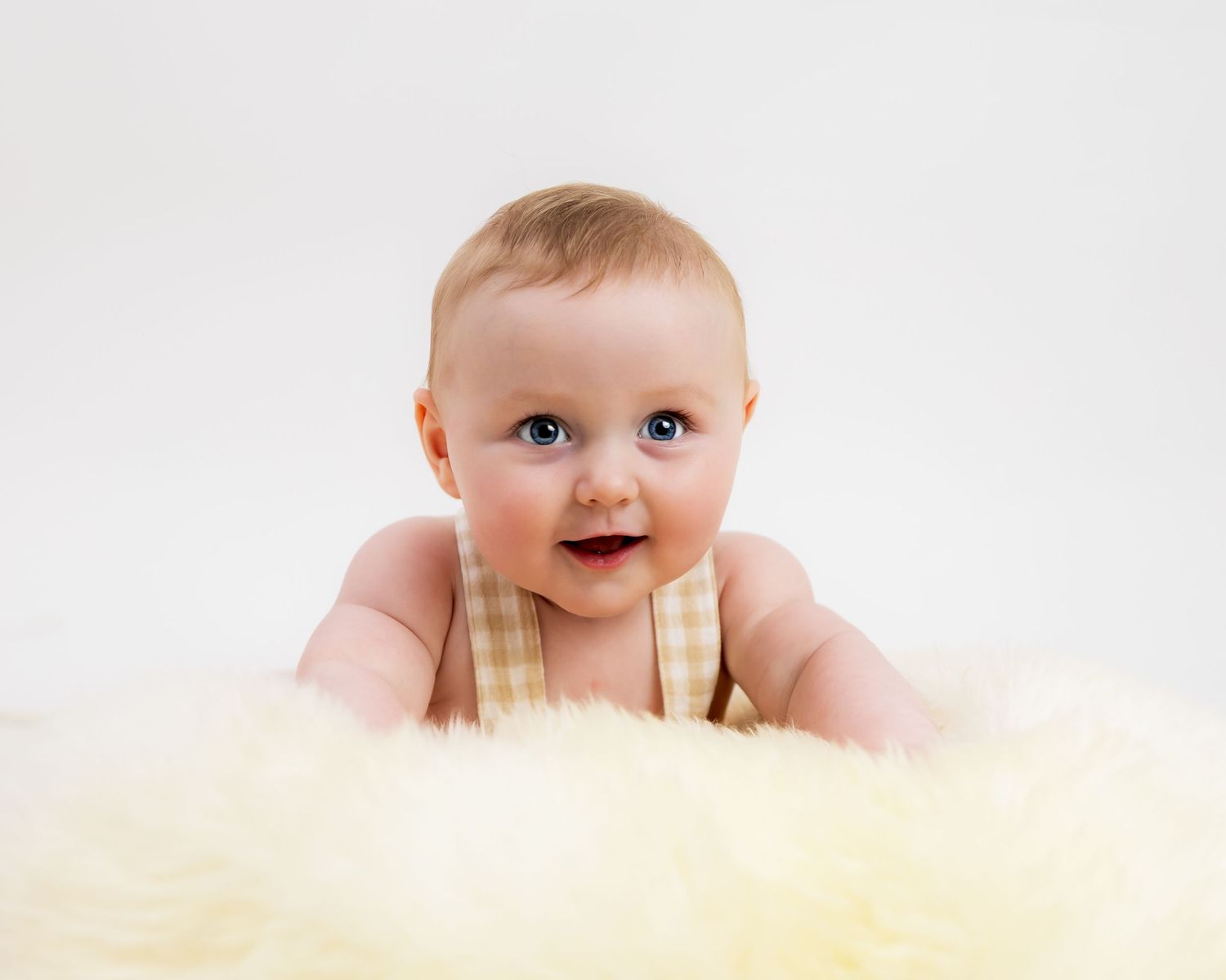 Baby peeking over edge of yellow fuzzy blanket with bright expression.