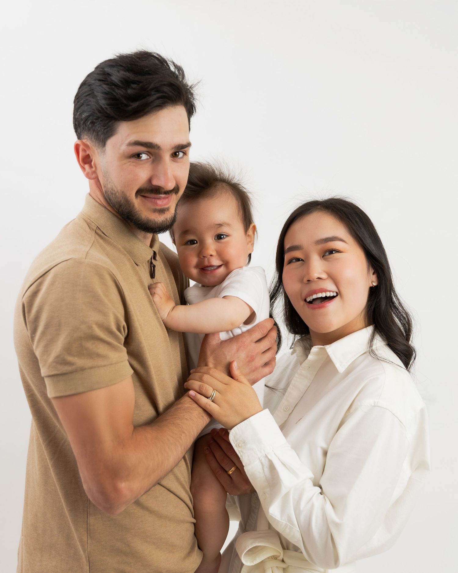 Family in coordinated white and tan outfits sharing an intimate moment on white background.