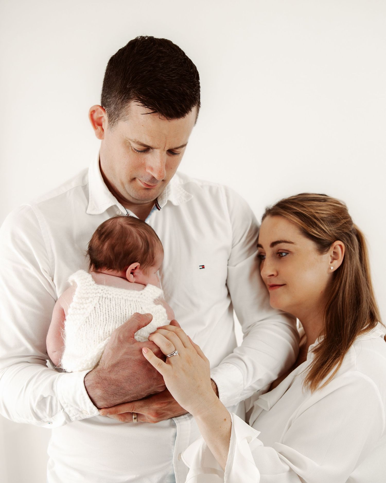 Tender family moments with newborn baby captured in white studio setting.