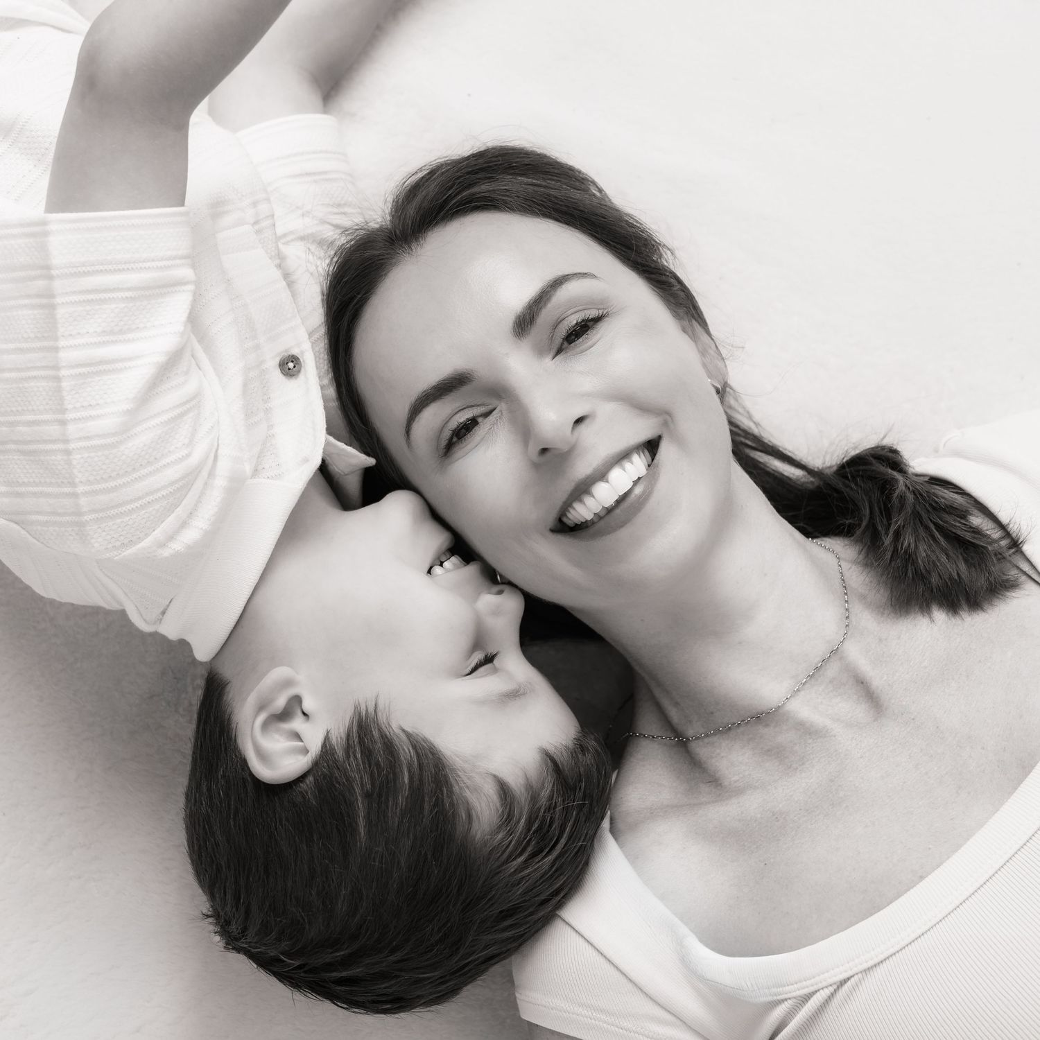 Black and white photo of a smiling woman and child lying down together, sharing a tender moment.