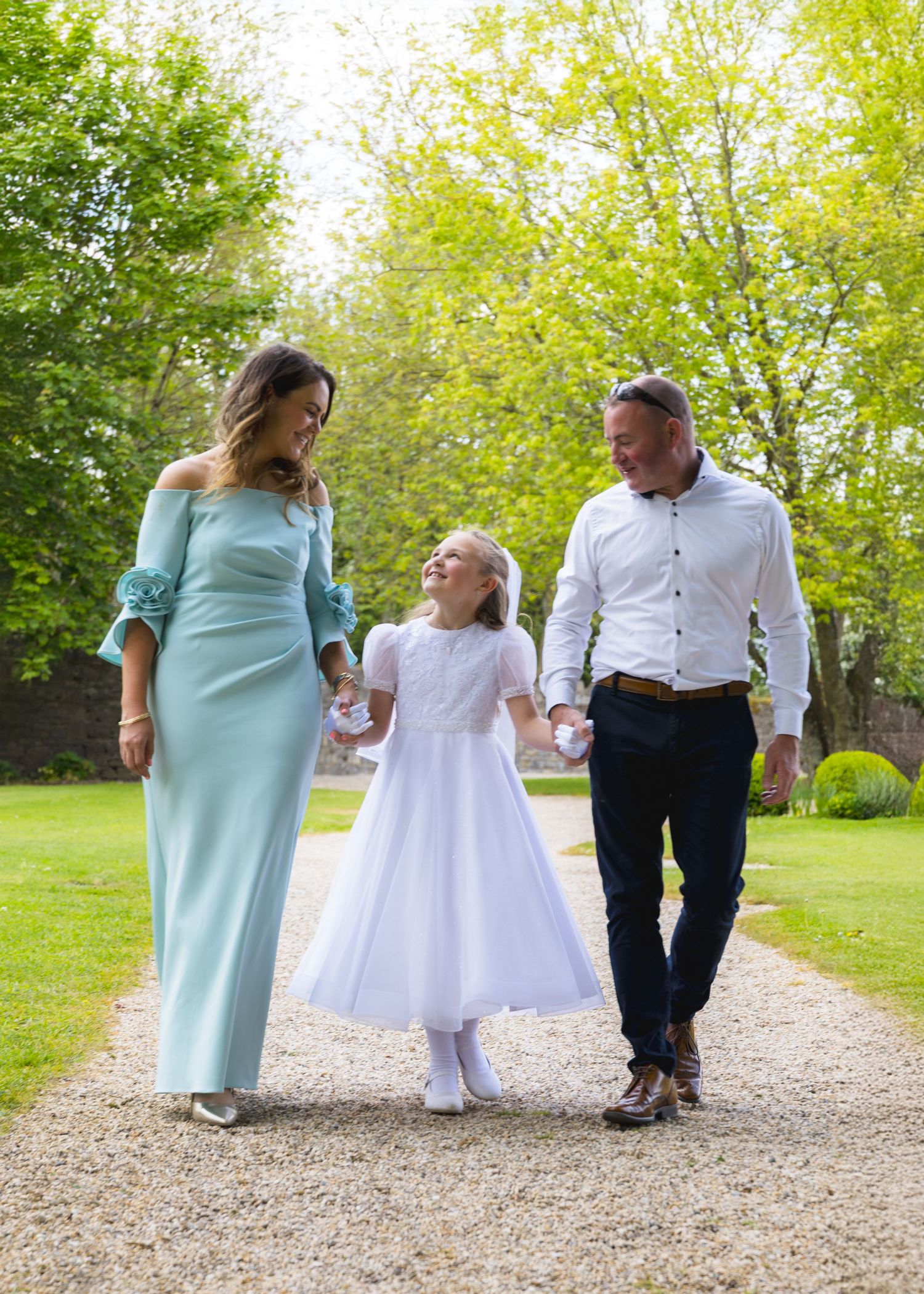 Family walking together on a gravel path in formal wear.