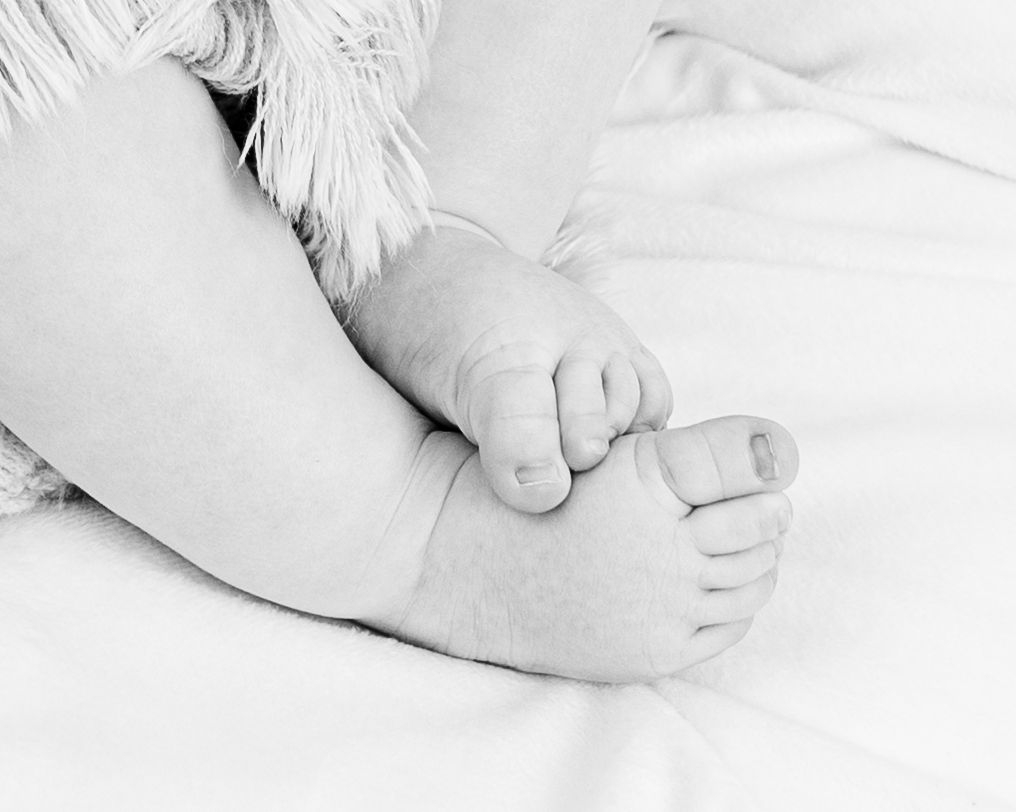 Black and white close-up photograph of tiny baby feet against white fabric.