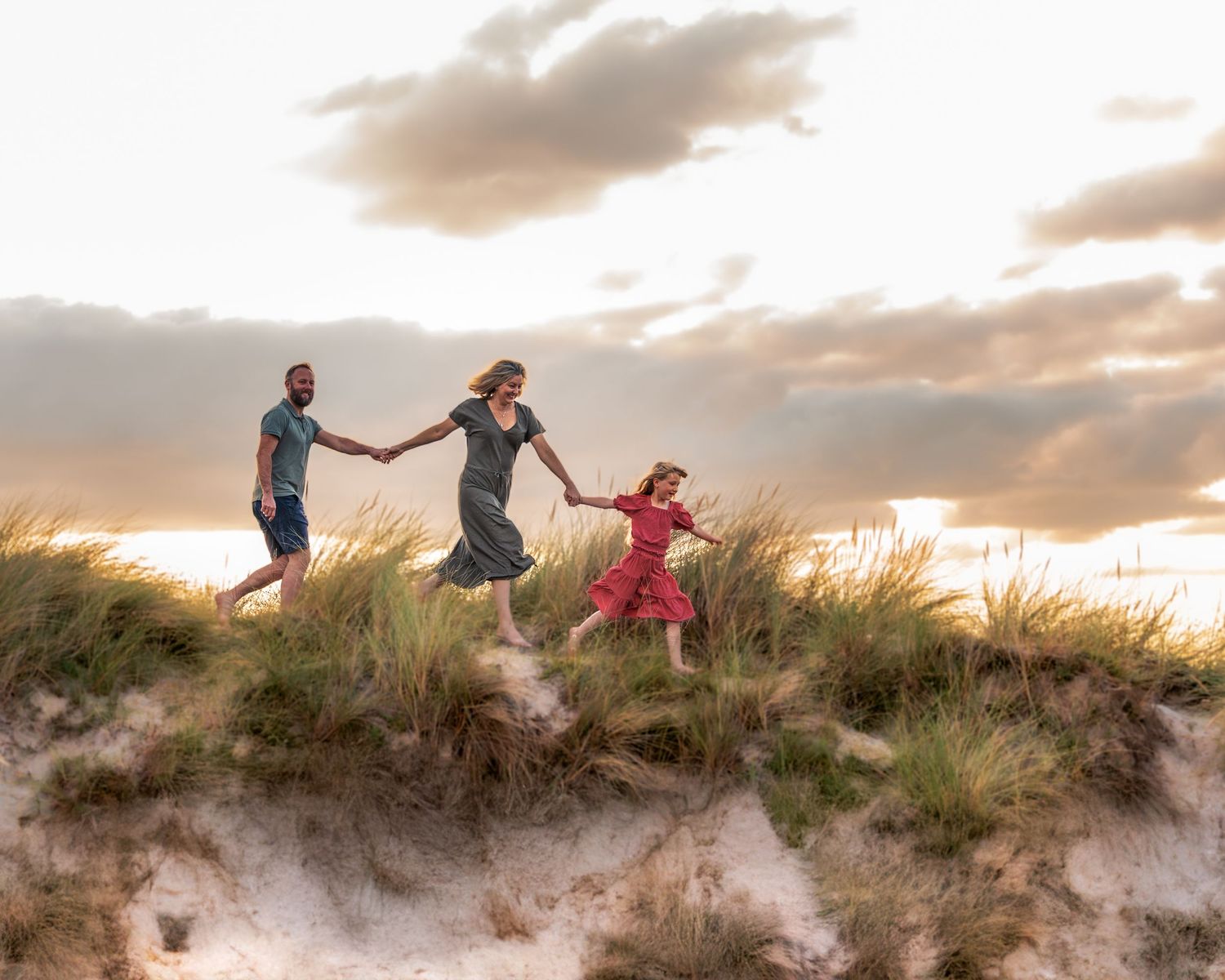 Group walking and playing on sandy dune ridge during sunset.