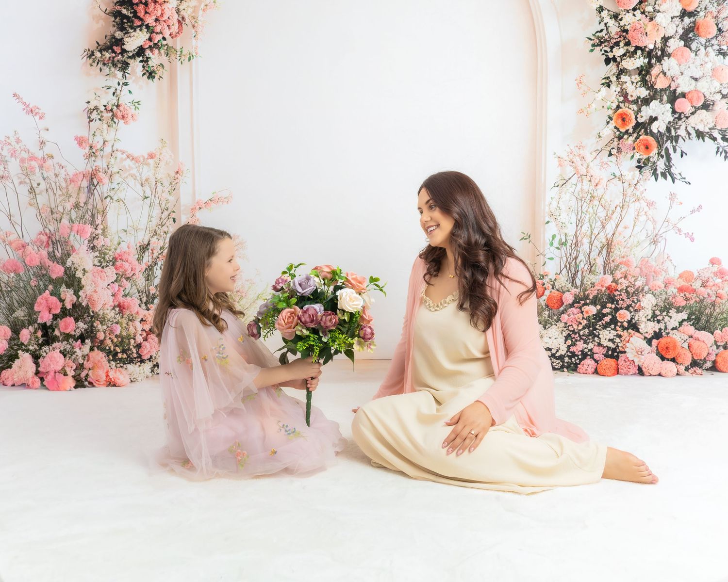 A dreamy photoshoot sequence featuring two people in soft yellow dresses surrounded by pink floral arrangements.