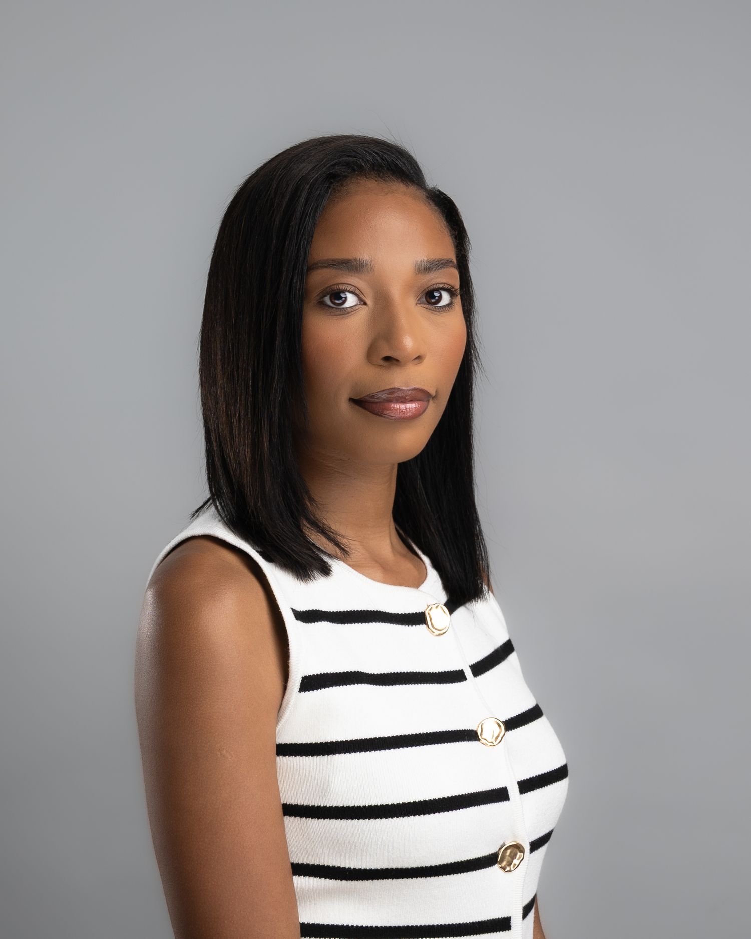Professional headshot of a woman in a black and white striped sleeveless top against a gray background.