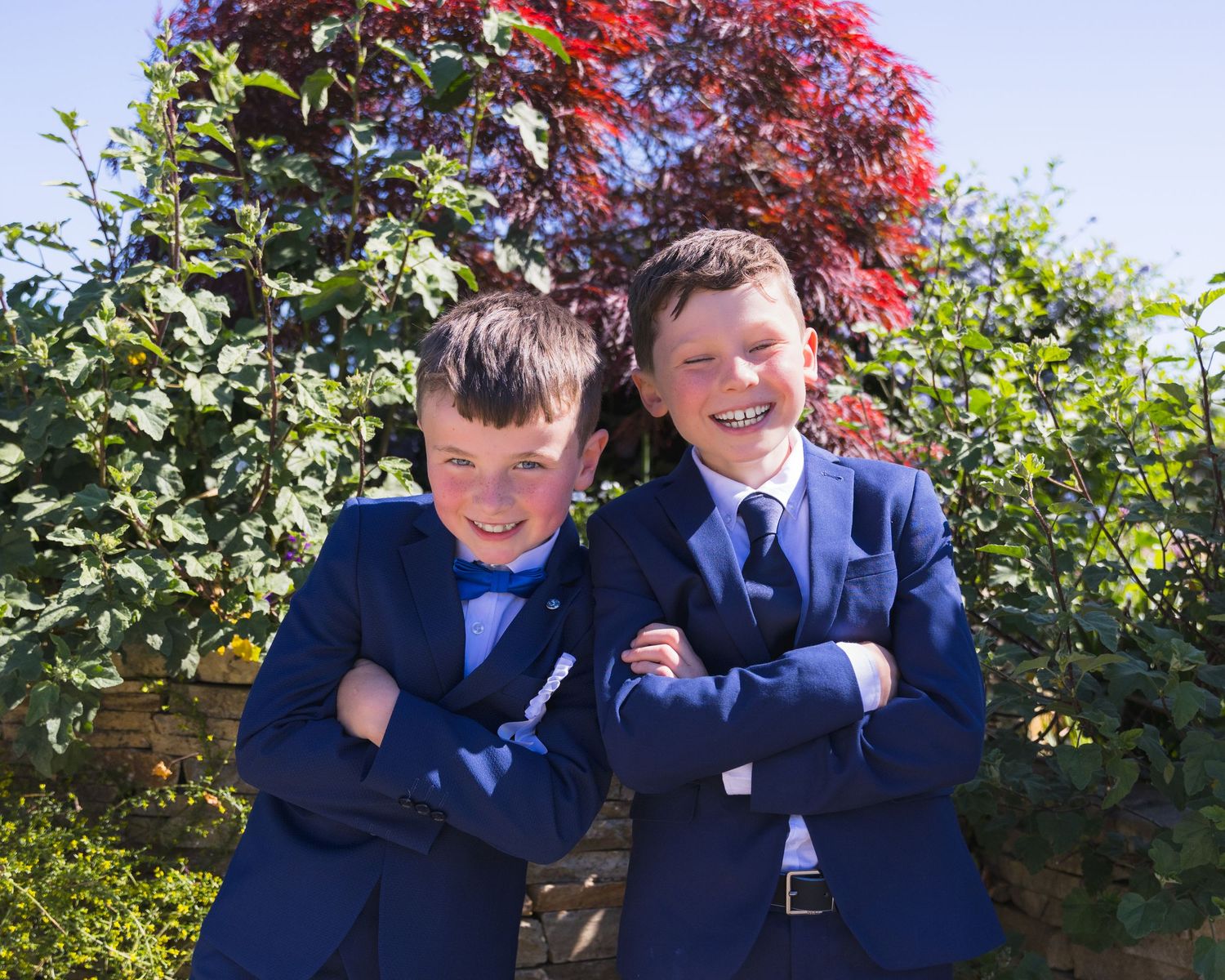 Children in navy blue formal attire posing together in a garden setting.