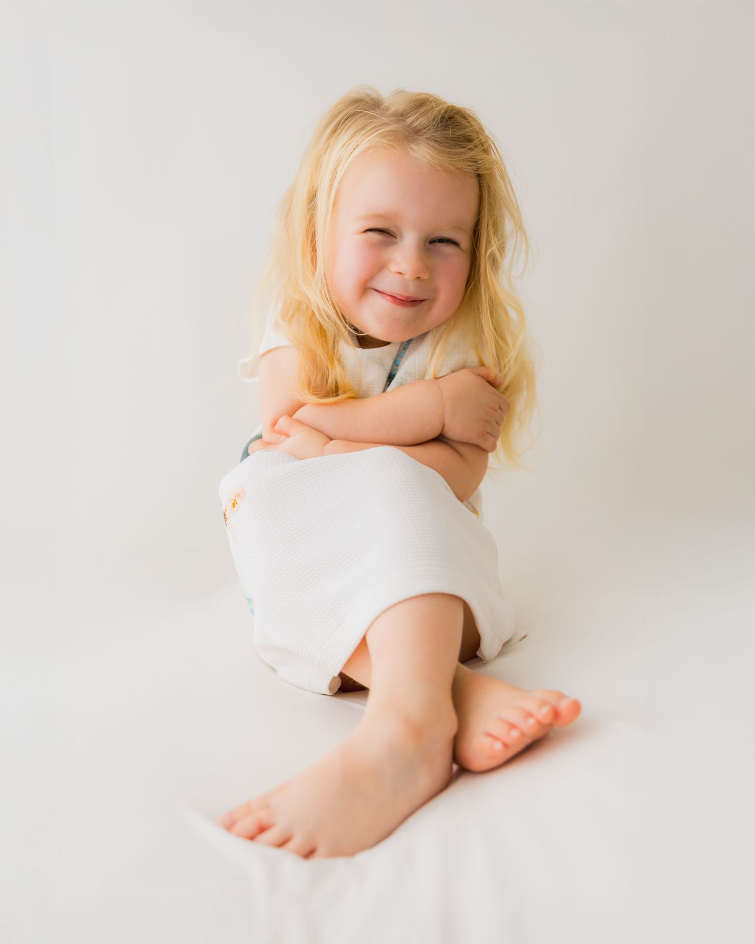 Joyful child lying on white bedding with bright smile.