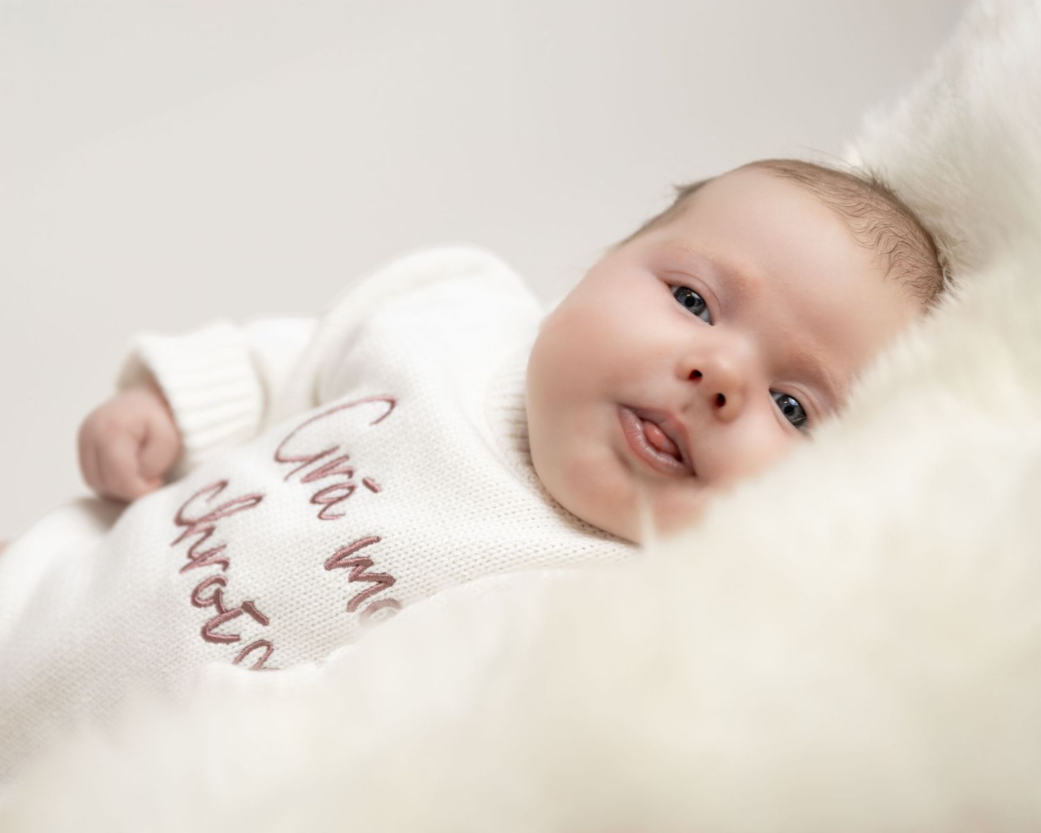 A baby lies peacefully on white bedding in a series of connected soft focus photographs.